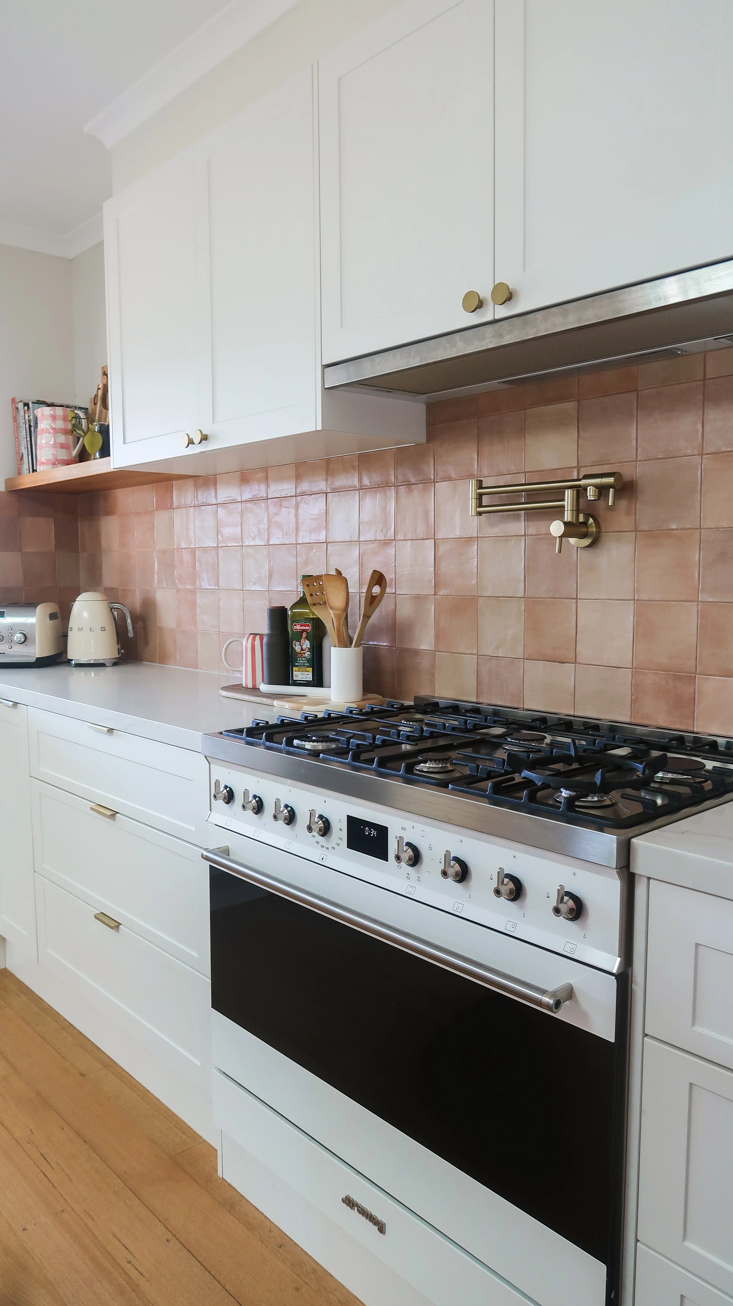 A modern kitchen with white cabinets, a beige backsplash, and a stainless steel oven with a gas cooktop. There are kitchen utensils, a toaster, a kettle, and some jars on the countertop.