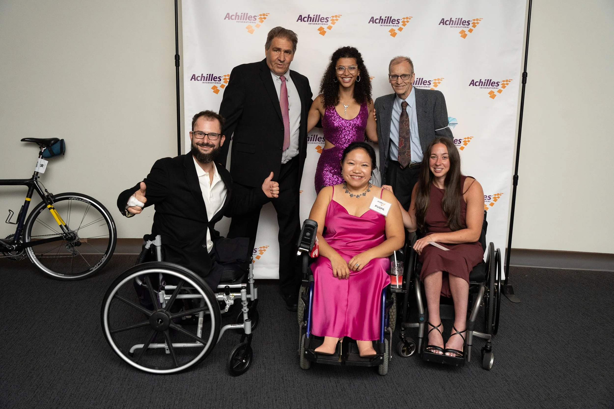  Group of athletes pose in front of Achilles branded step and repeat  