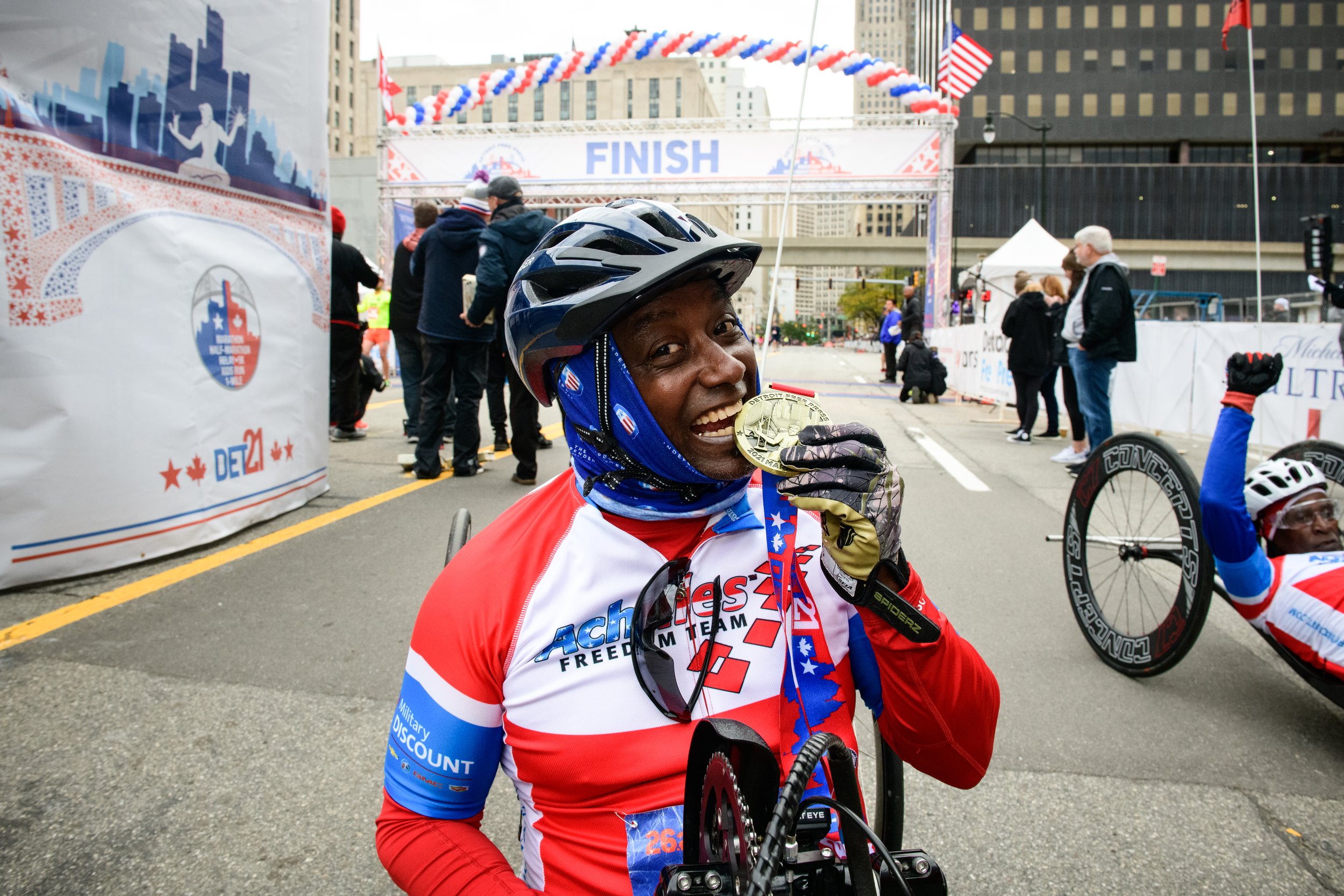  Photo of Achilles Freedom Team member biting his medal at the 2021 Detroit Marathon  