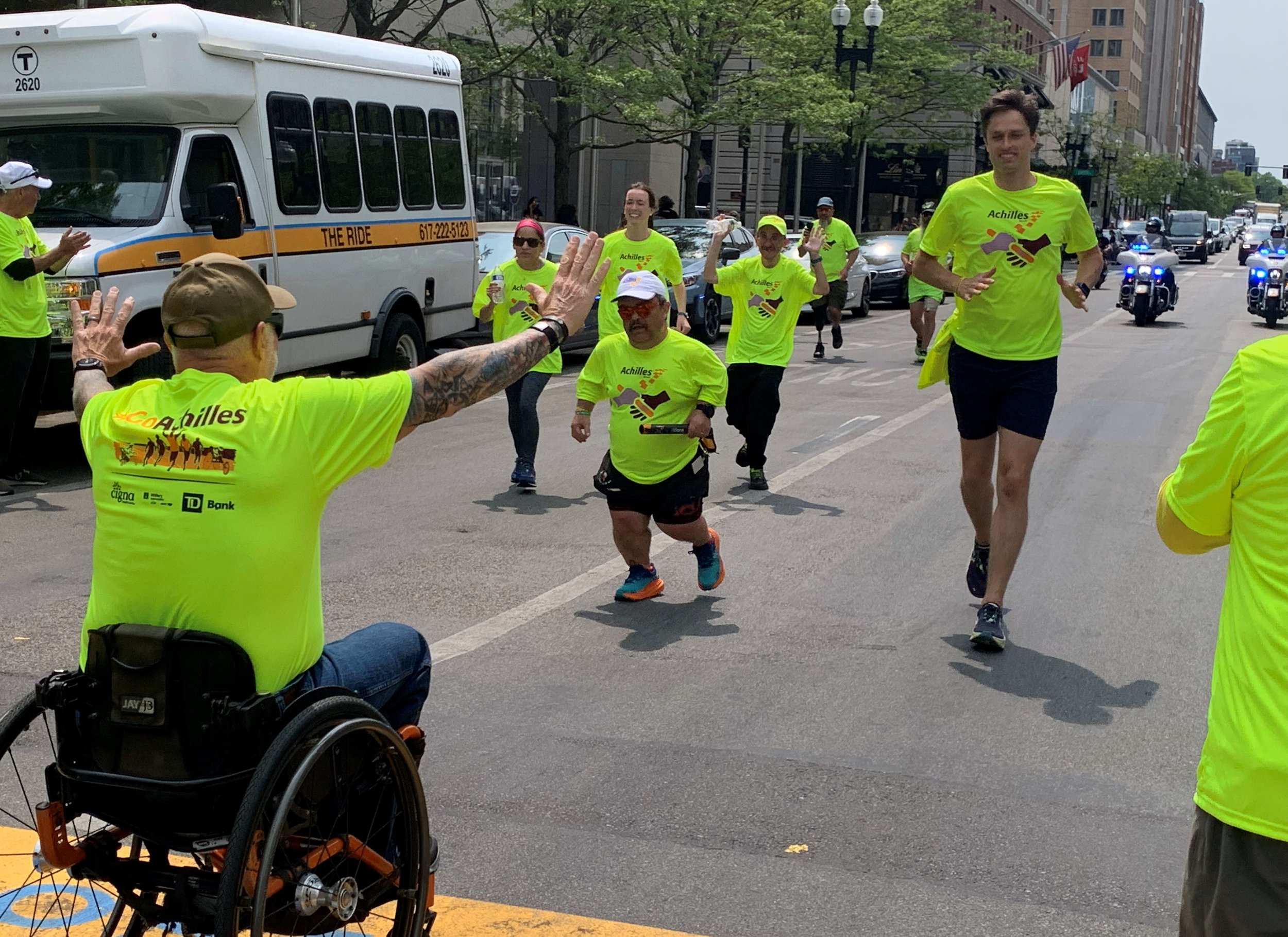  Achilles member in a wheelchair cheering on another Achilles member who is about to cross the finish line 