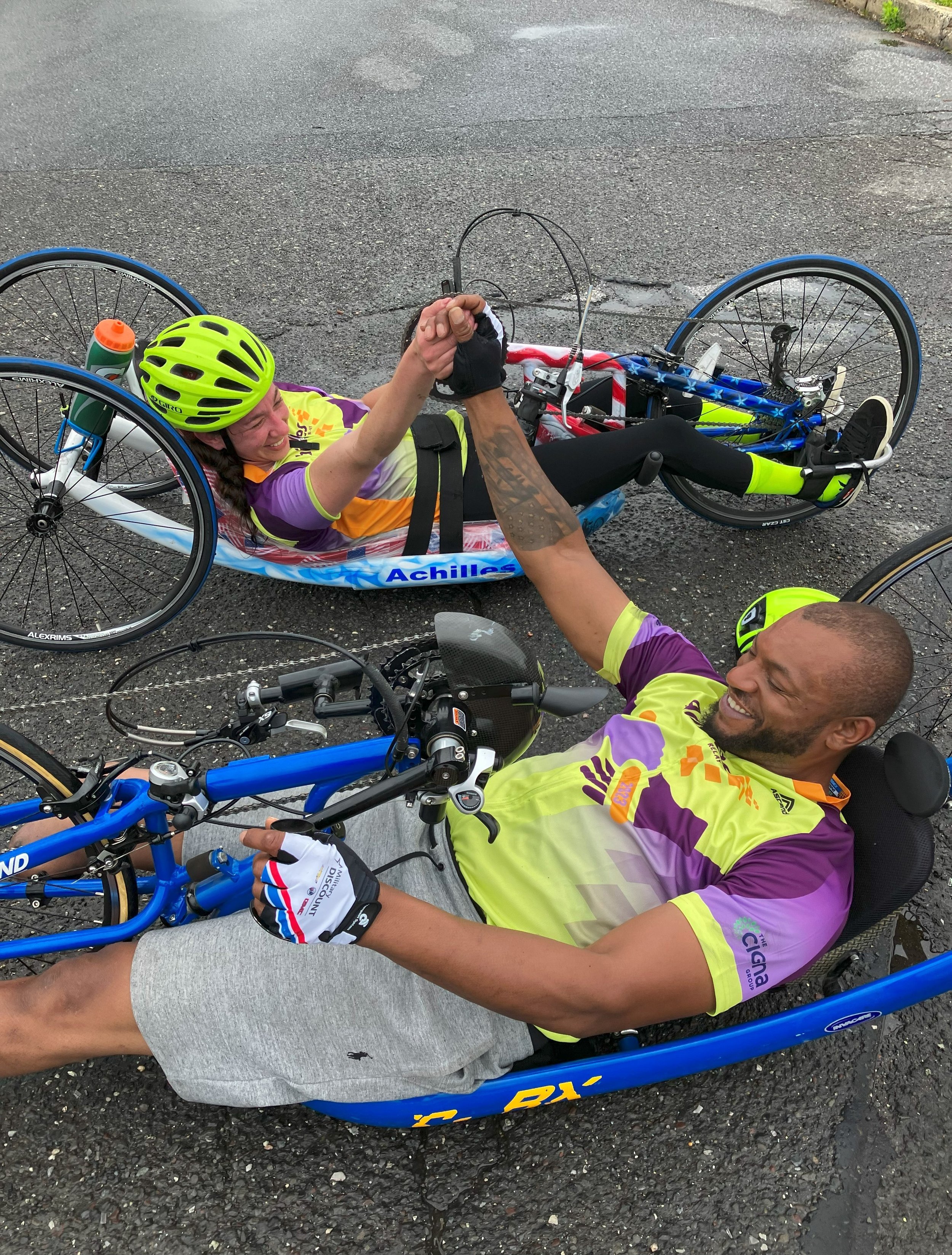  Achilles handcycle athletes holding hands while sitting on their handcycles  