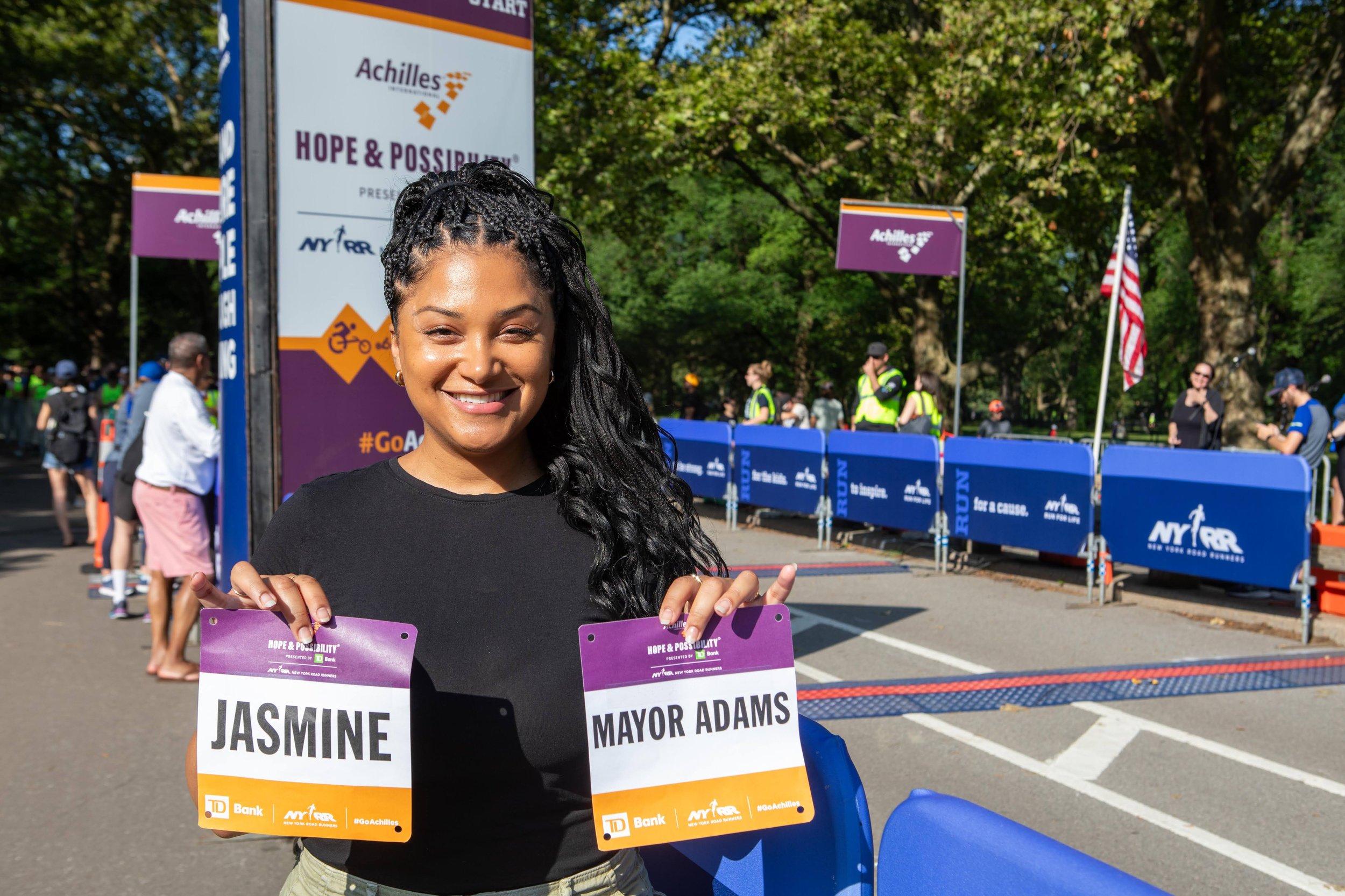  Jasmine Ray holding two race bibs that read “Jasmine” and “Mayor Adams” 