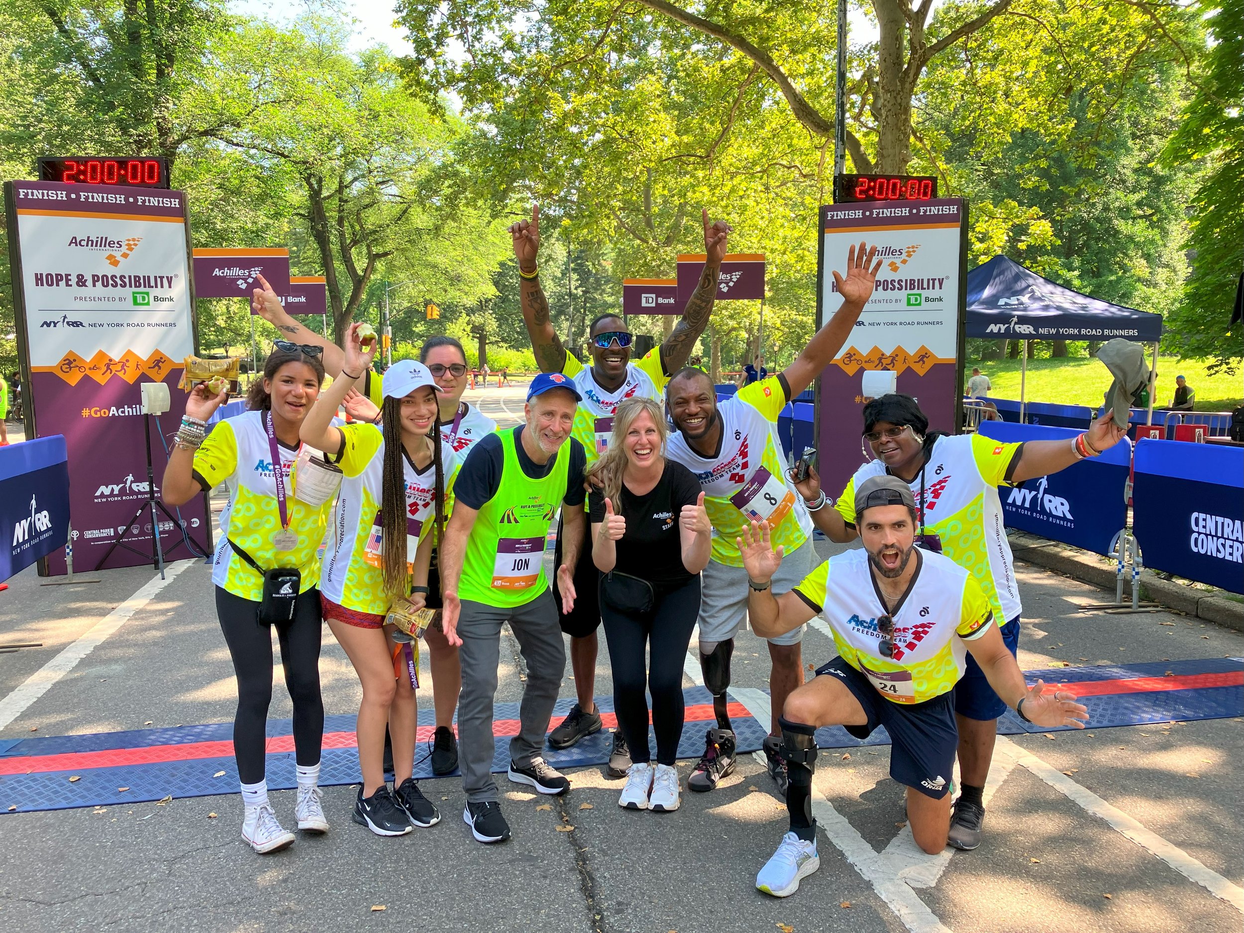  Group shot of members of the Achilles Freedom Team cheering at the finish line with Jon Stewart and Janet Patton, Director of the Achilles Freedom Team 