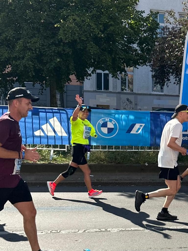  Achilles member smiling and waving while running on the Berlin Marathon race course.  
