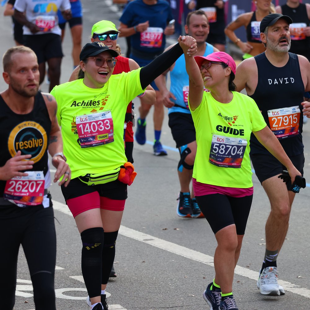  Achilles athlete and guide holding hands and smiling together on the NYC Marathon race course 