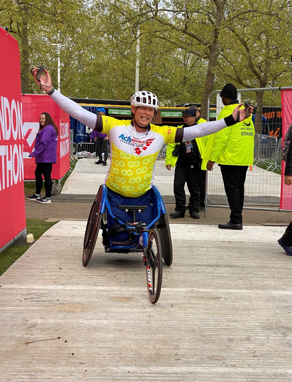  Achilles Freedom Team athlete cheering with his arms outstretched in his racing wheelchair  