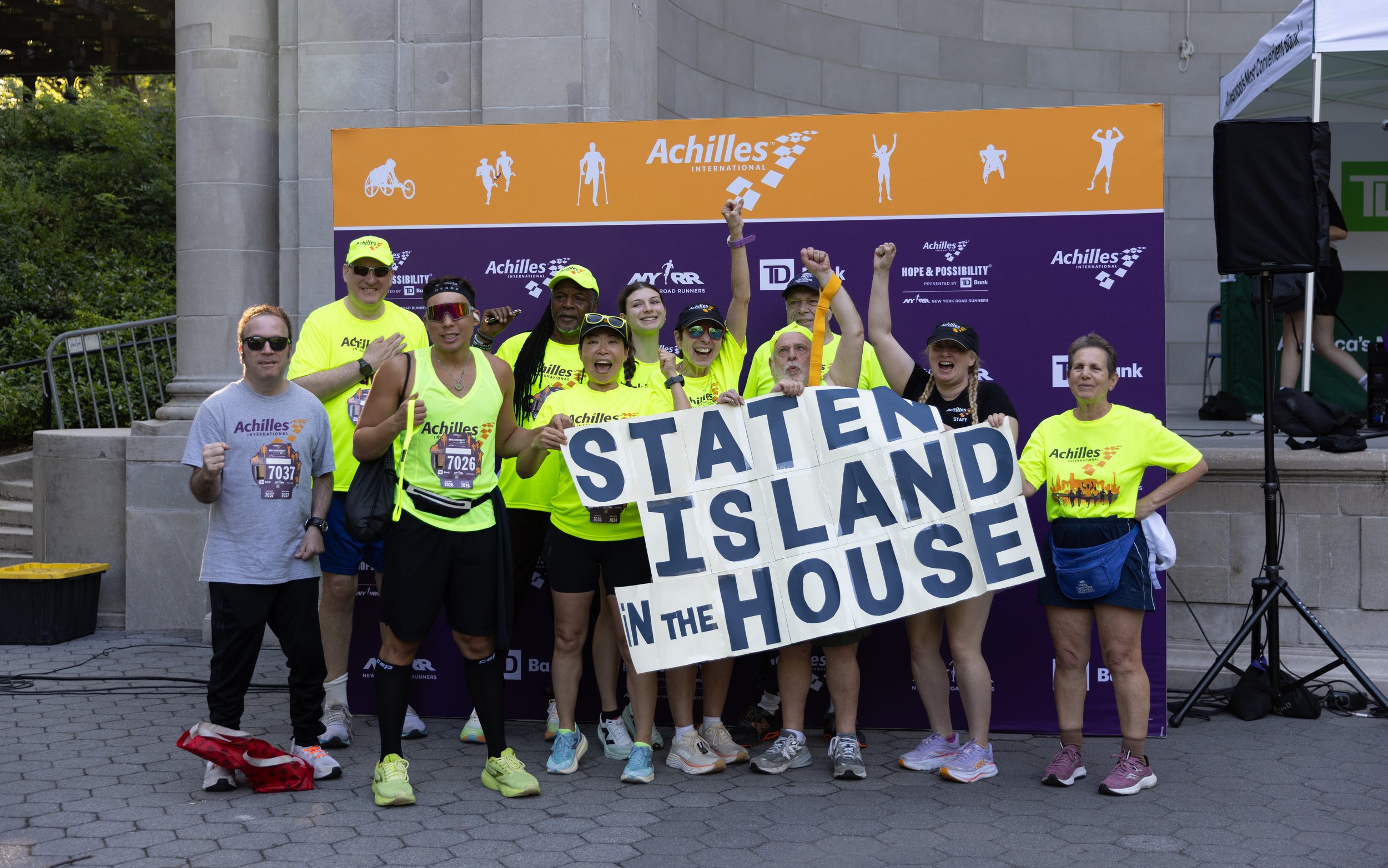Group photo of Achilles Staten Island athletes in the festival area with a sign that reads “Staten Island in the house.”