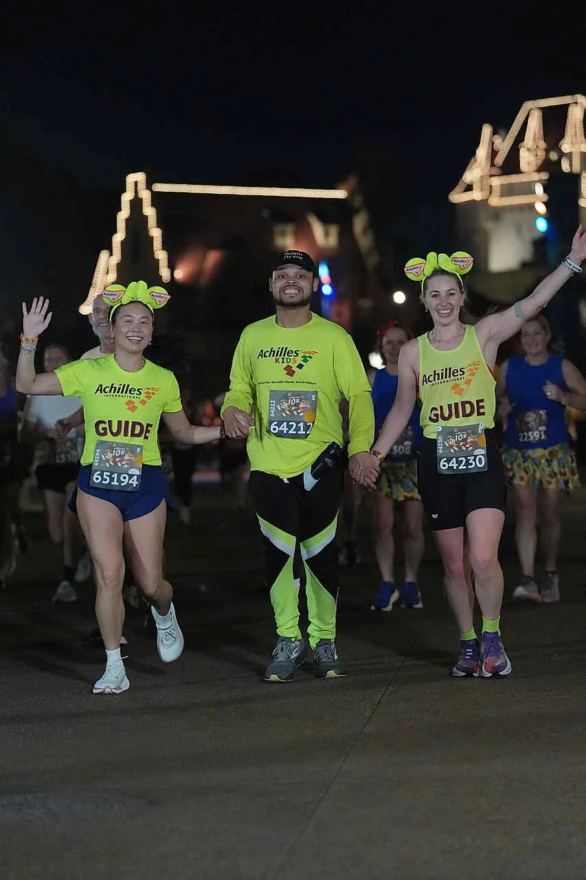  Achilles Kids member holding hands with his guides as they all cheer together.  