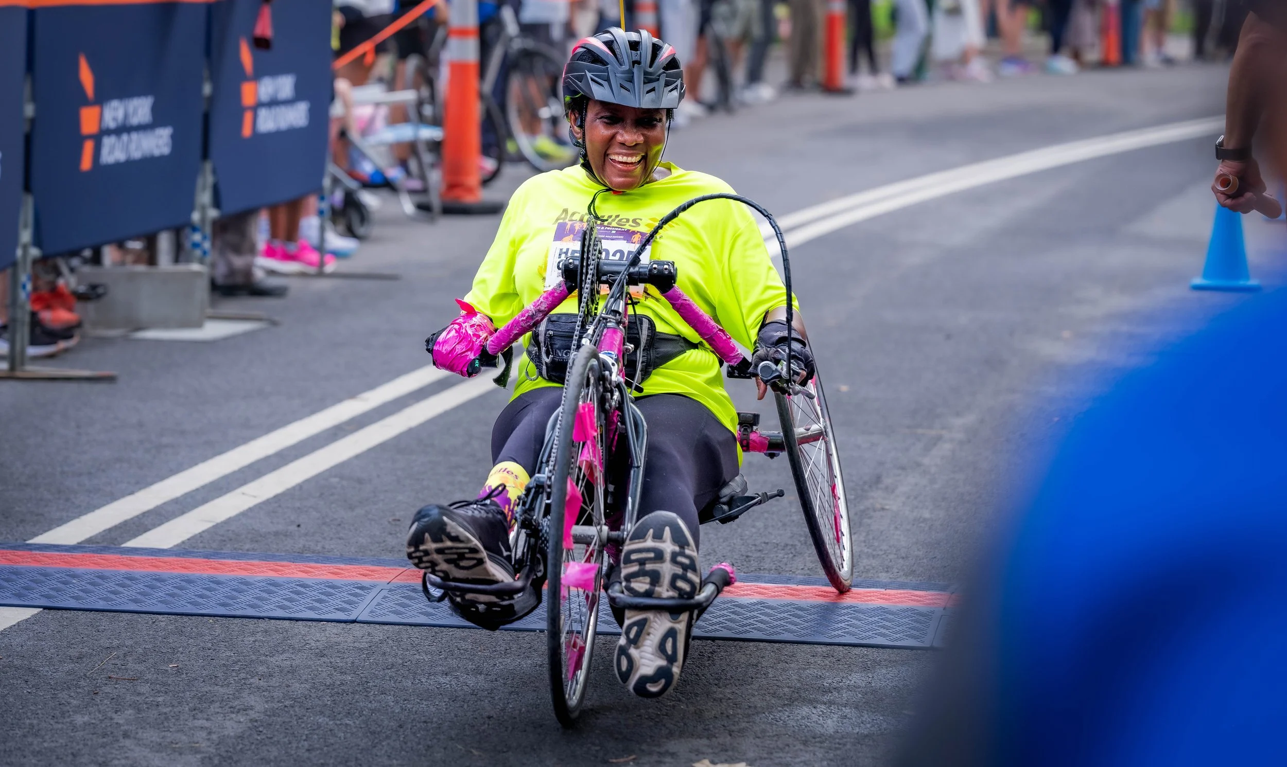  Achilles athlete smiling as she crosses the finish line on her handcycle.  