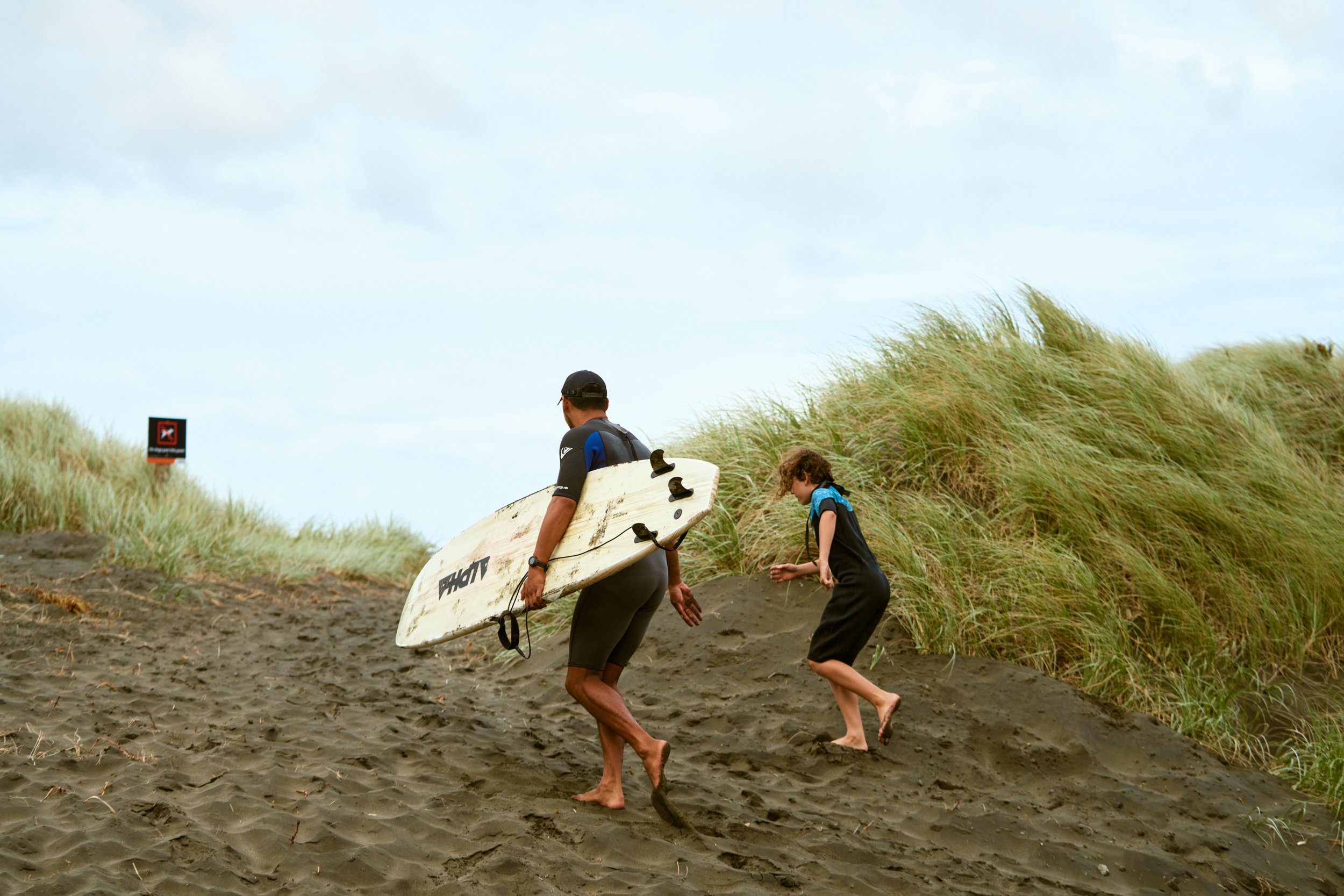 Lead Surf Coach and Founder of PIPI Surfmate, Kaylib Heke, taking a kid to an ocean surf lesson at Muriwai Beach in March of 2022.