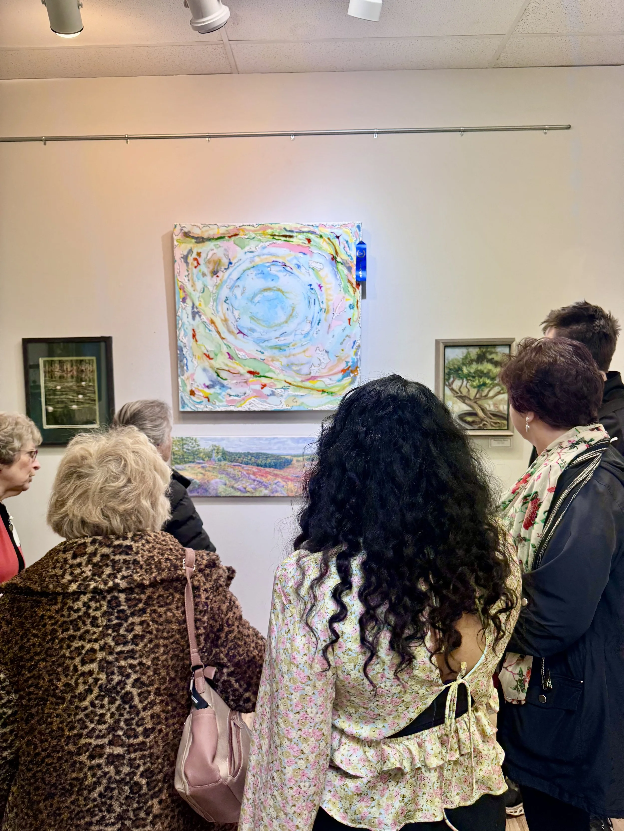 Group of people viewing colorful abstract paintings in an art gallery.