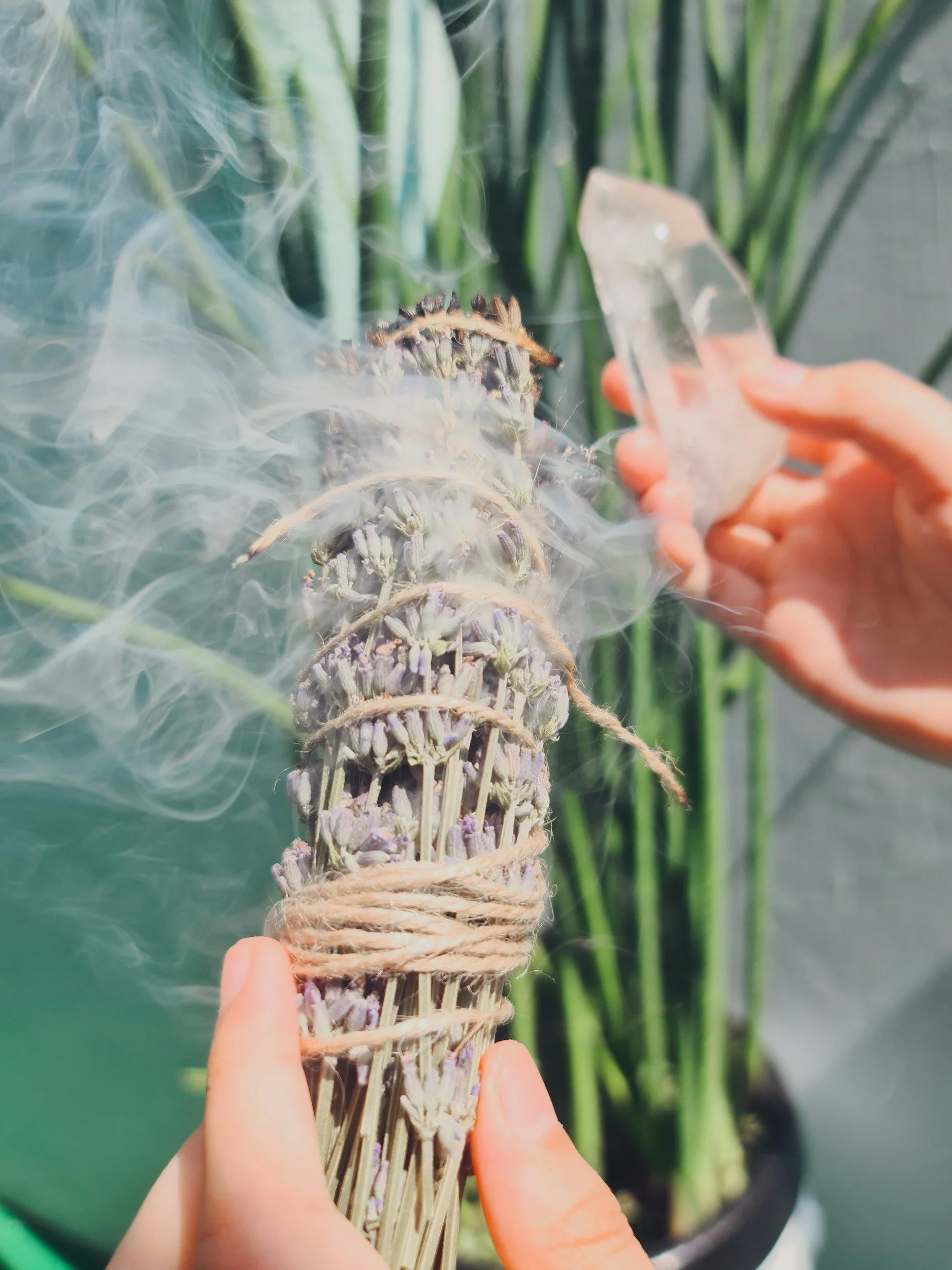 Someone holding a bundle of dried lavender tied with twine and releasing smoke or vapor from it.