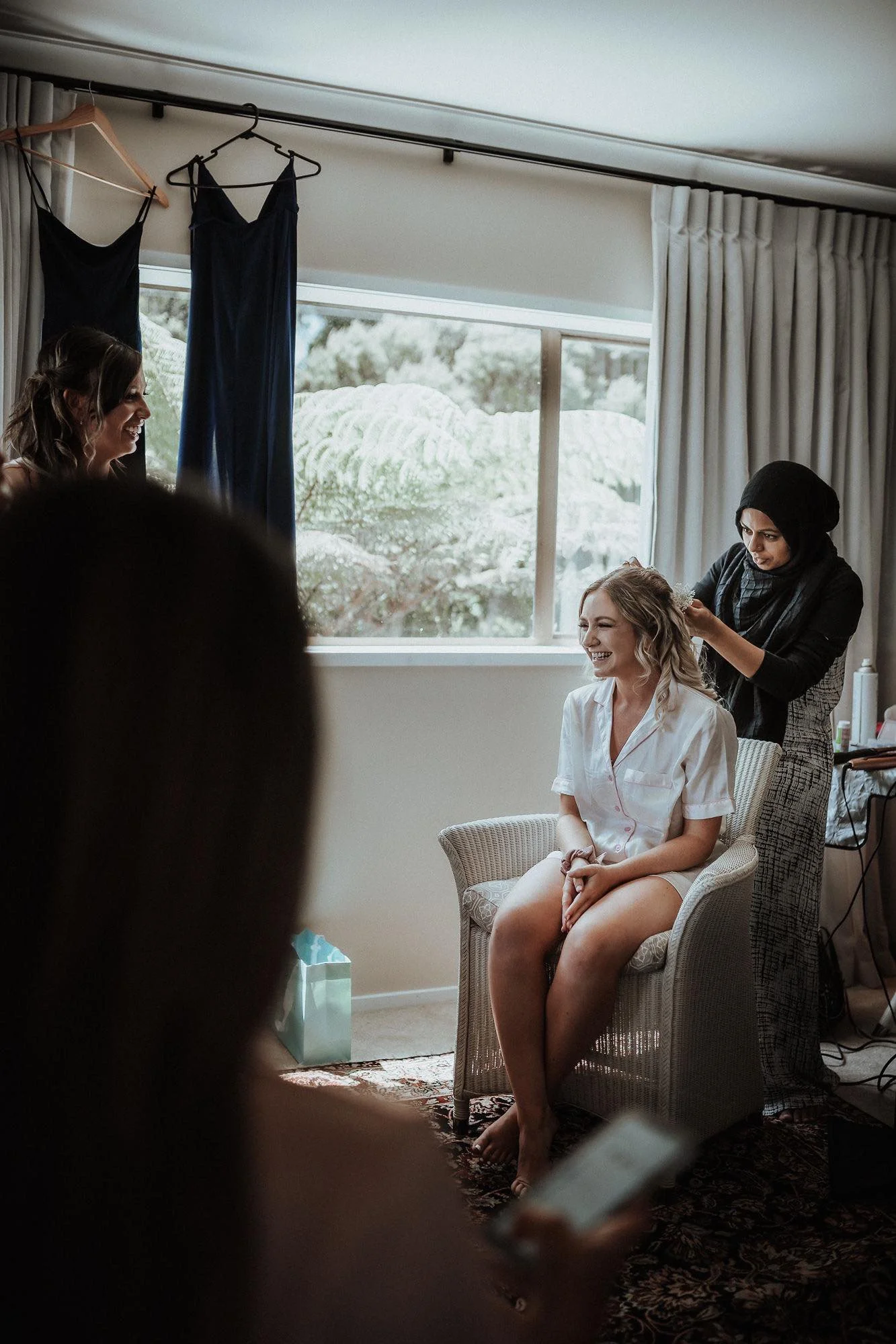 Bride Selena is smiling on her wedding day with her bridesmaids as bridal hairstylist finishes her wedding day hairstyle