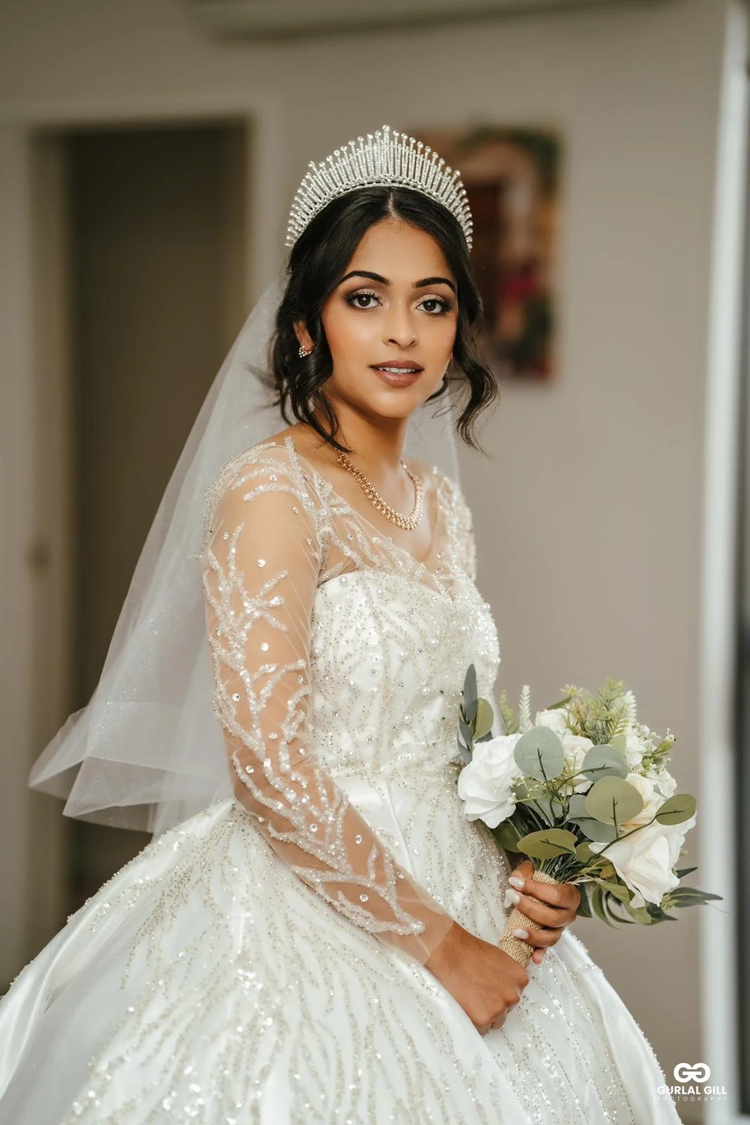 Indian catholic bride looking regal in her wedding gown on her wedding morning with a makeup look to compliment her tan skin tone and an updo bridal bun hairstyle with face framing pieces
