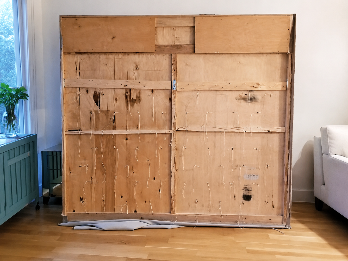 Exposed wooden rear structure and tufting cords of an oversized upholstered headboard during disassembly