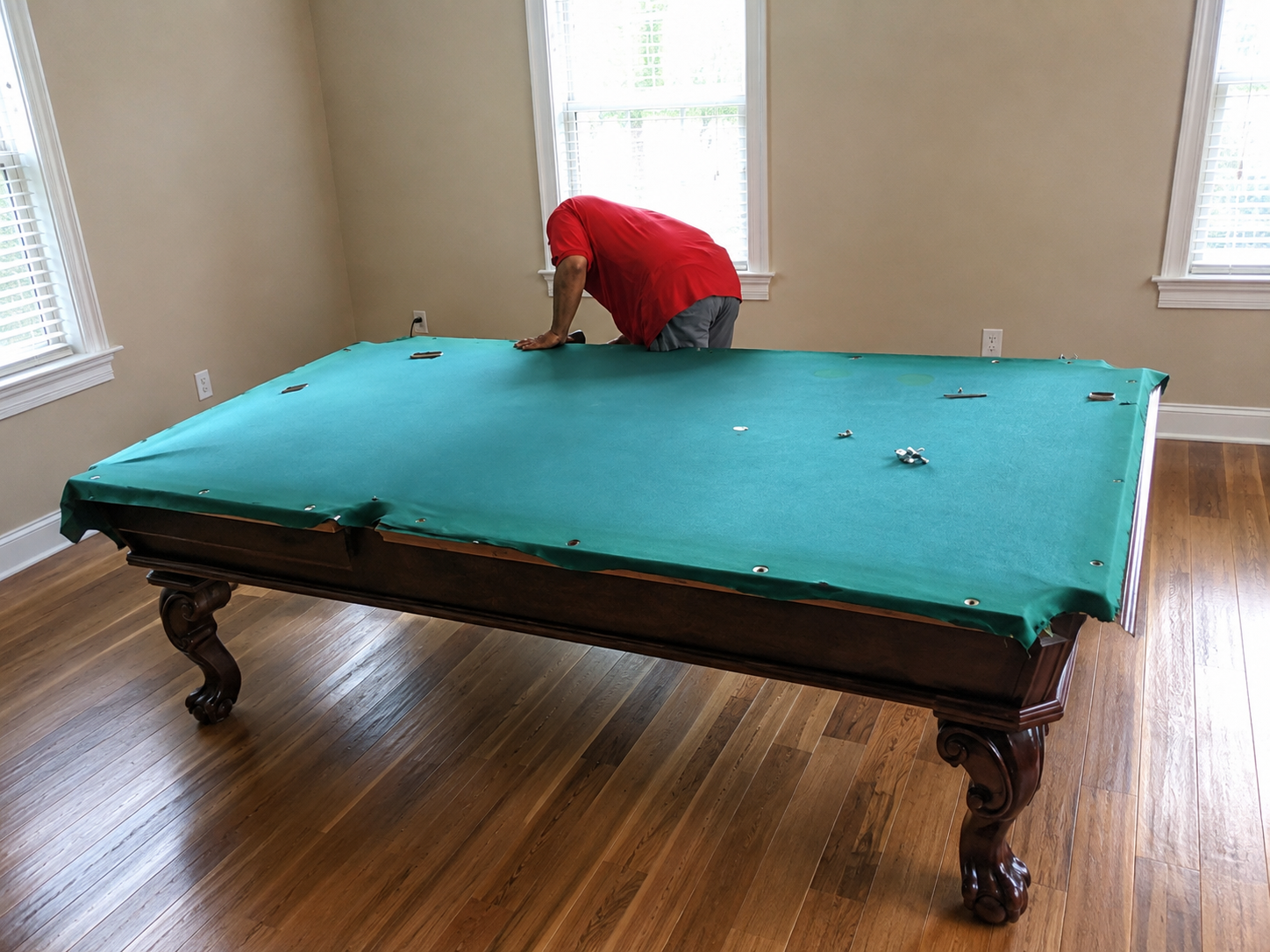 Technician positioning green felt while professionally reassembling a traditional wooden pool table