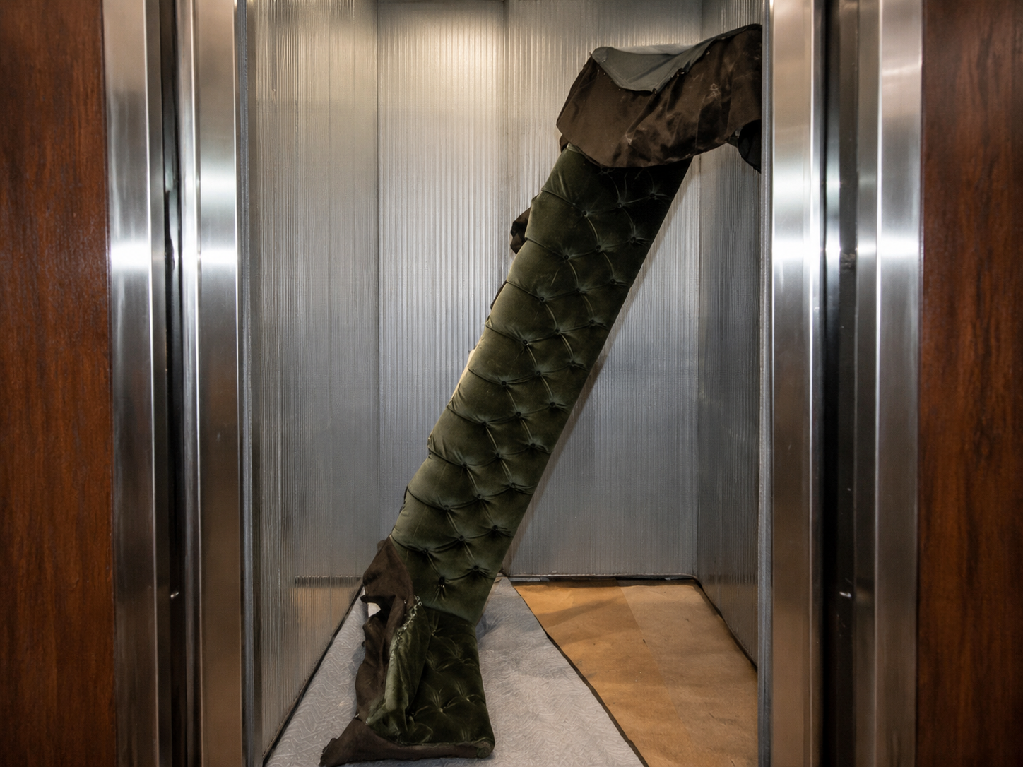 Tufted green velvet sofa component positioned inside a narrow elevator during professional moving service
