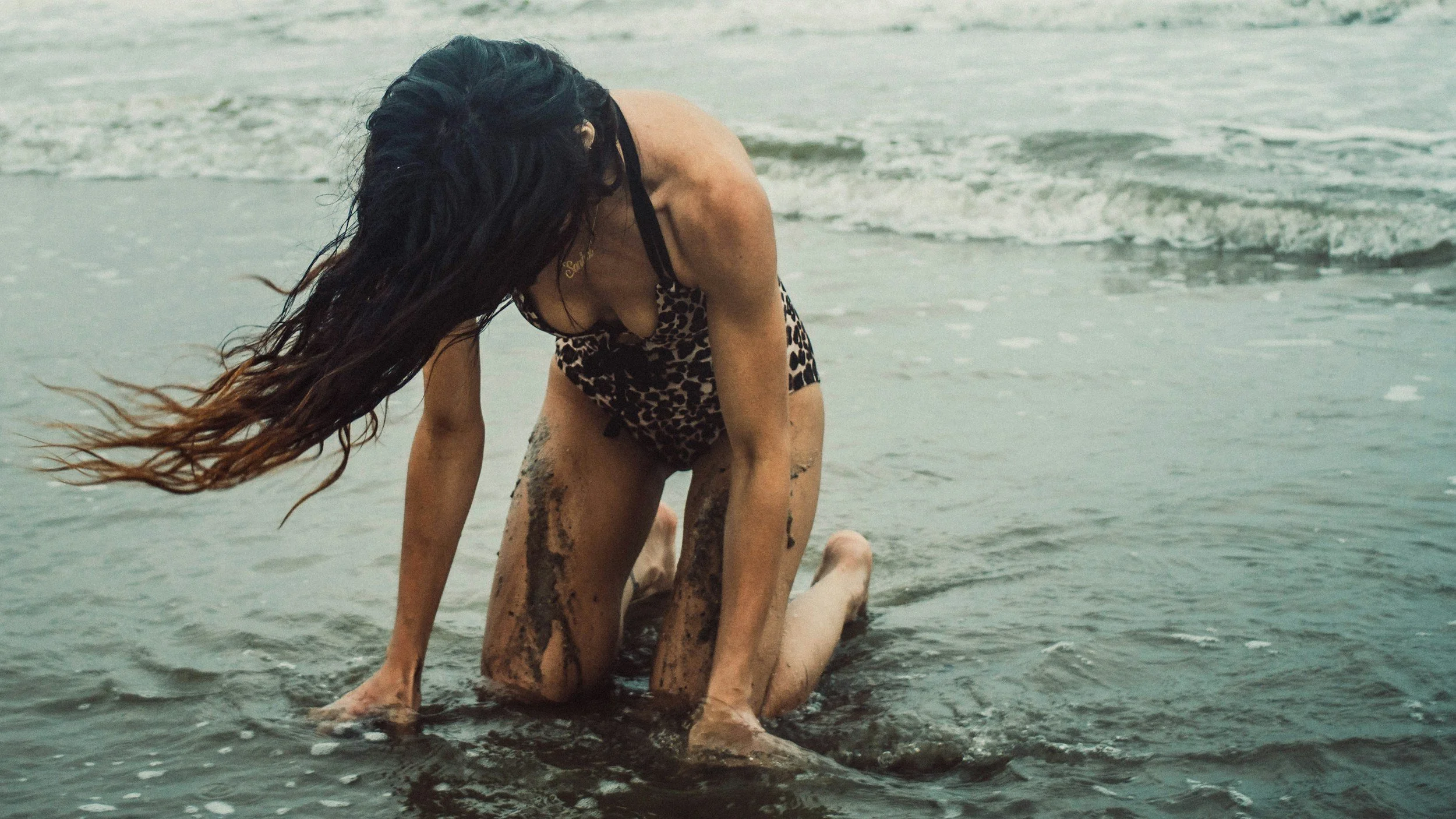 Woman kneeling on the sand with the ocean stretching out behind her