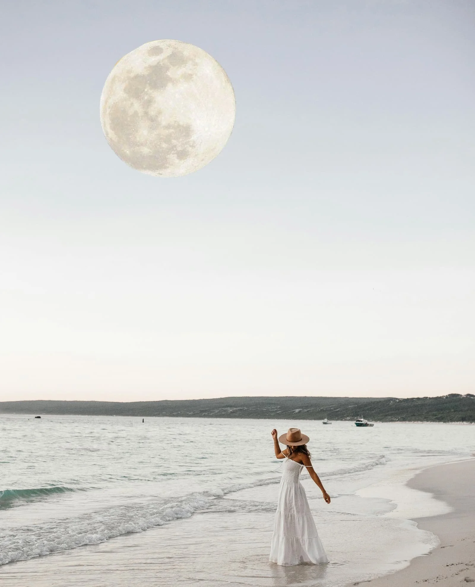 Woman in a white dress standing on the beach, the ocean and full moon behind her