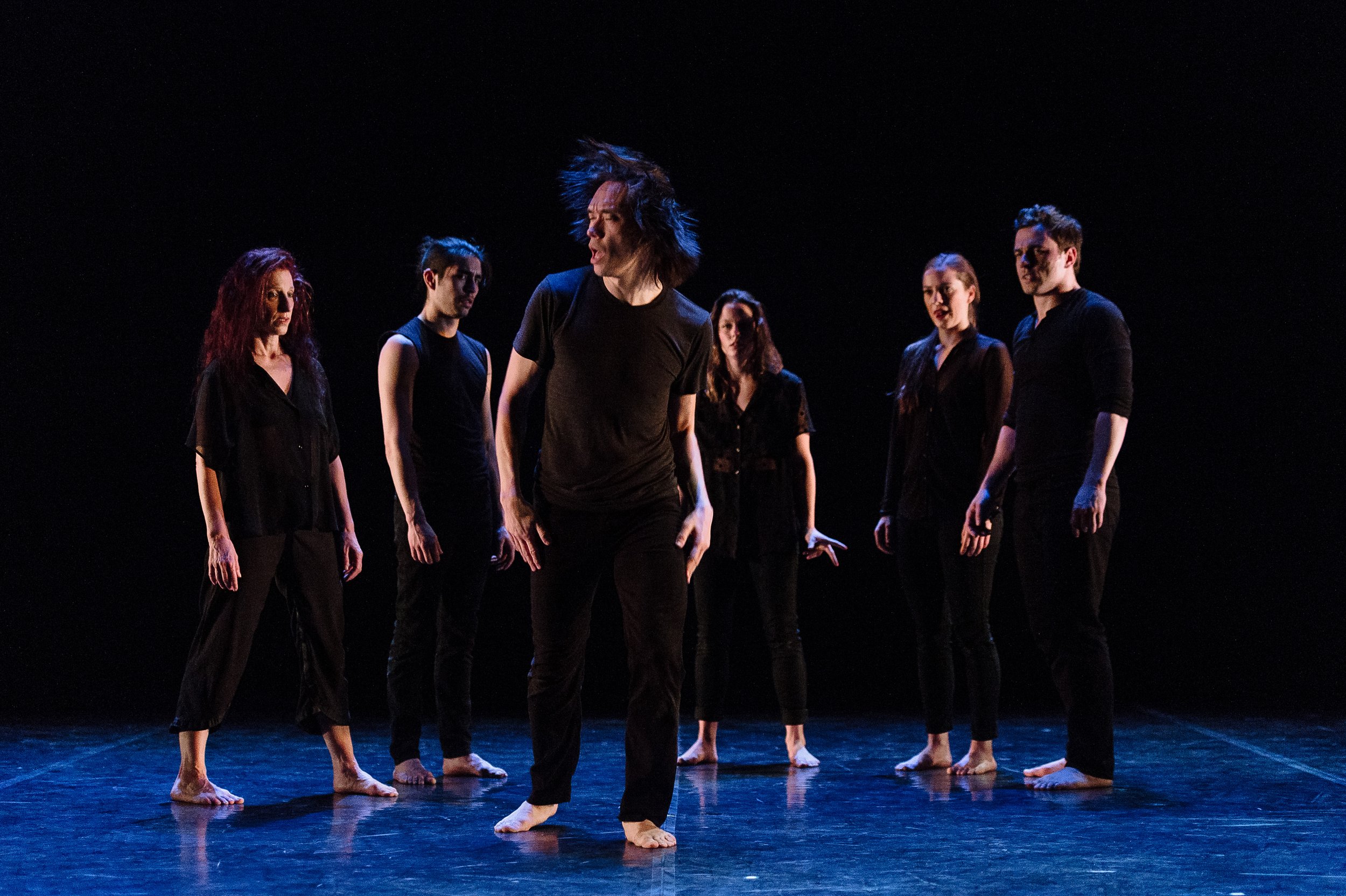 A group of dancers stand in a line; one steps forward from the rest.