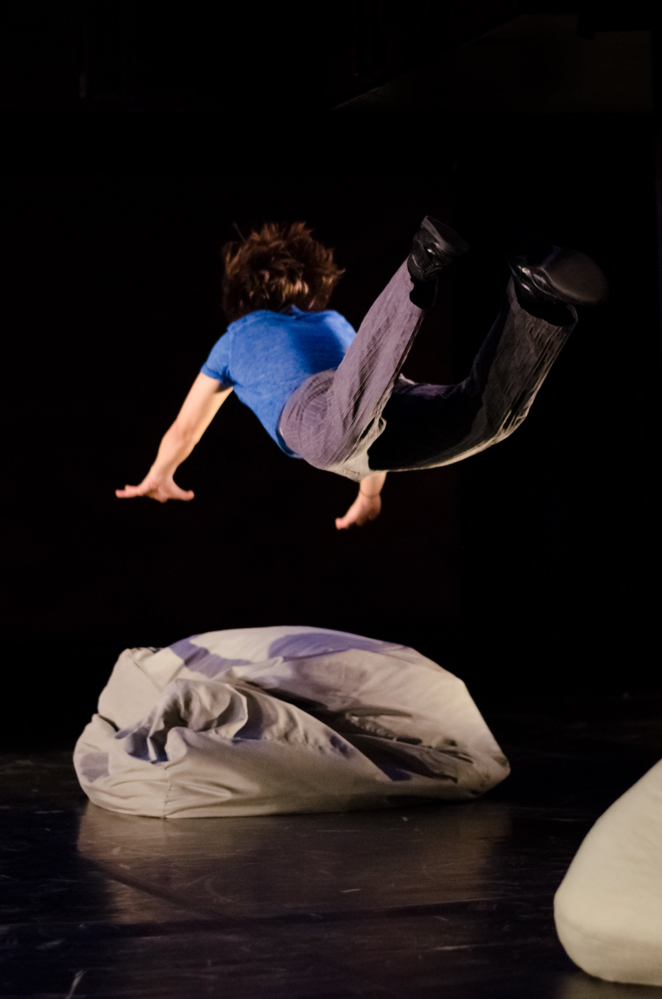 A dancer in mid air moving towards a beanbag chair.