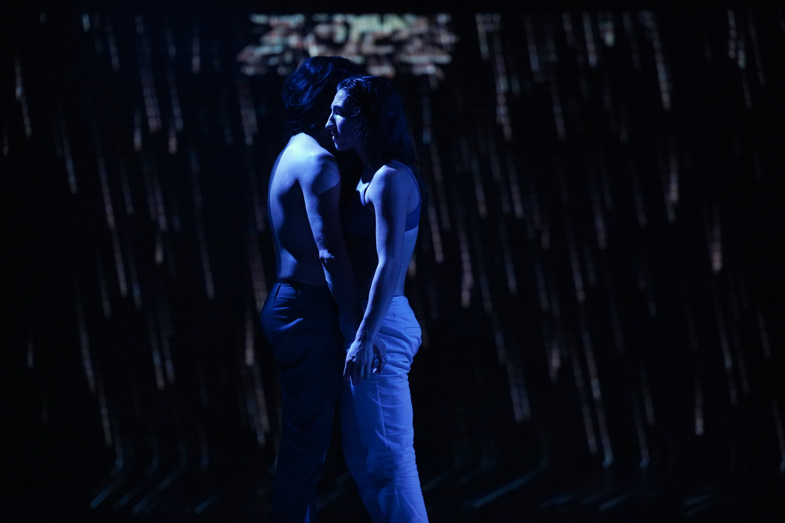 Mateo and Katherine stand shirtless with their  bodies almost touching.
