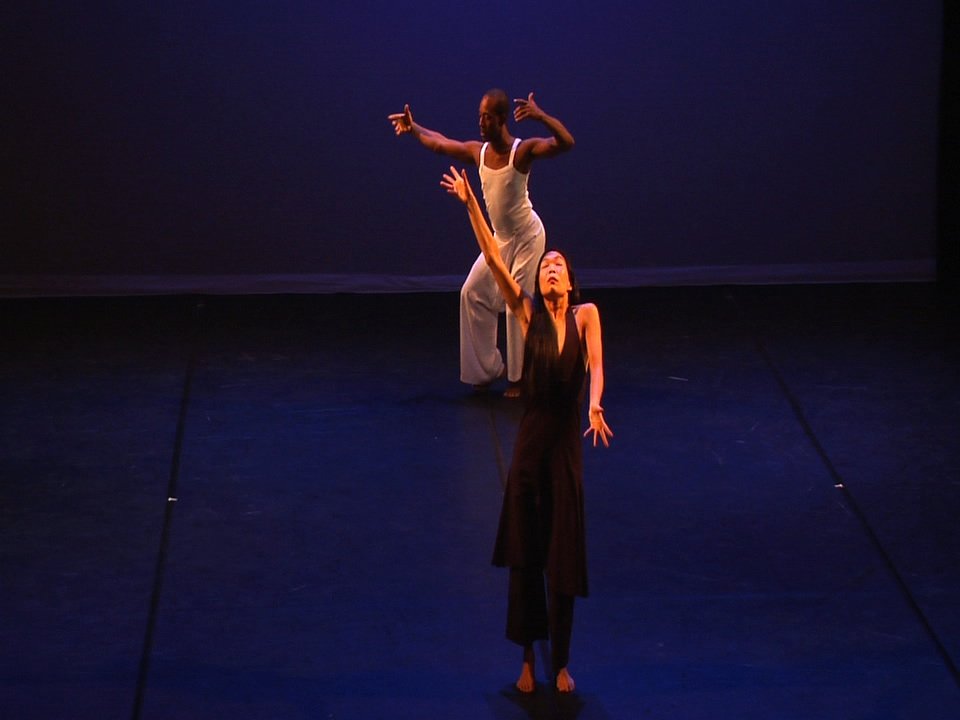 One dancer reaches an arm over head, another dancer extends an arm to one side.