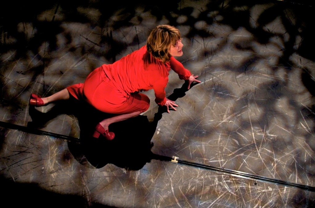 A dancer in a red top, skirt, and high heels crawls on a stage.