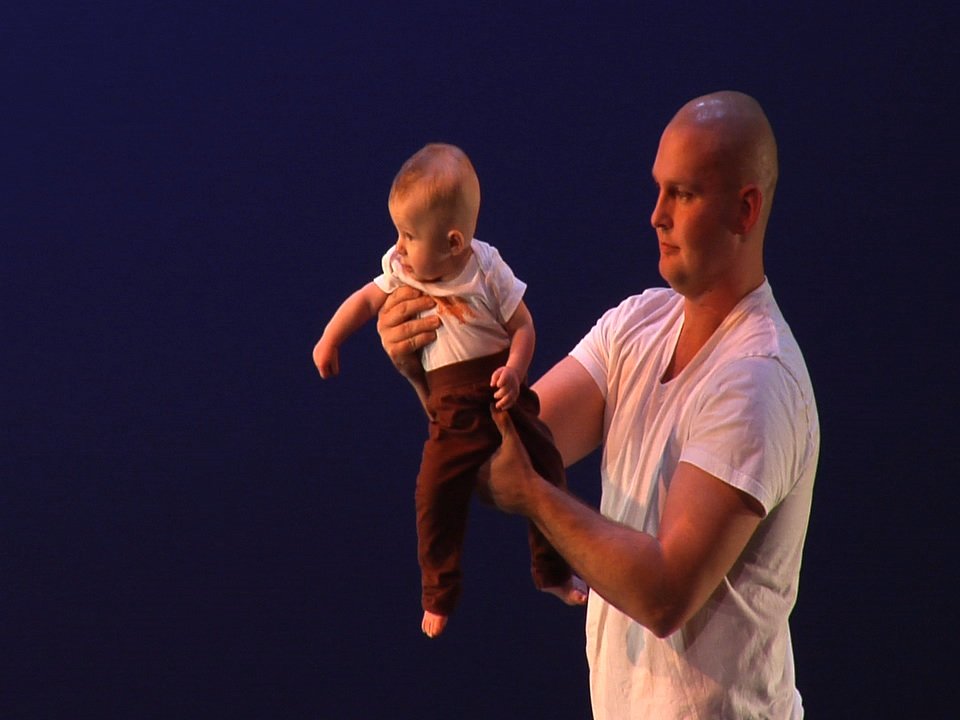 A dancer holds a baby out in front of them.