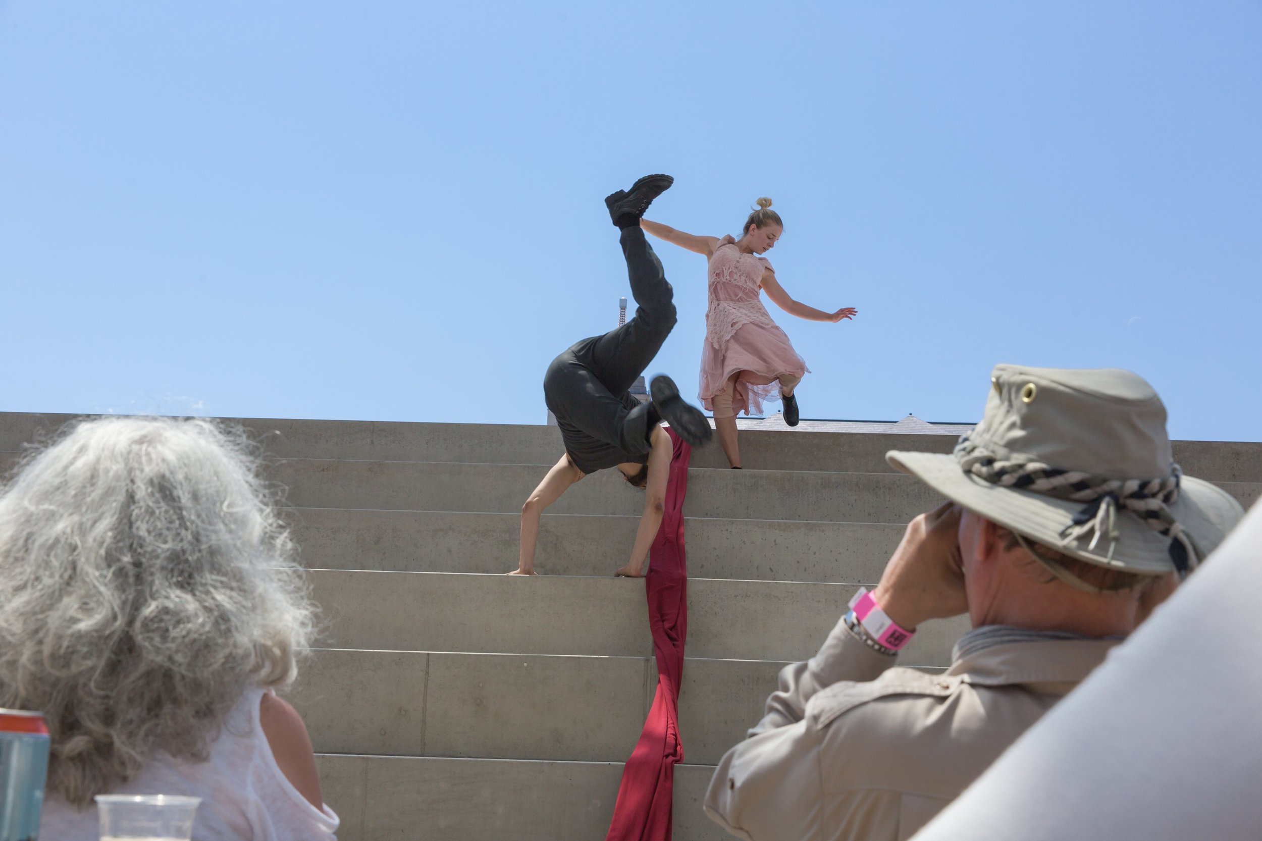 One dancer does a handstand on some steps while another runs down the steps.