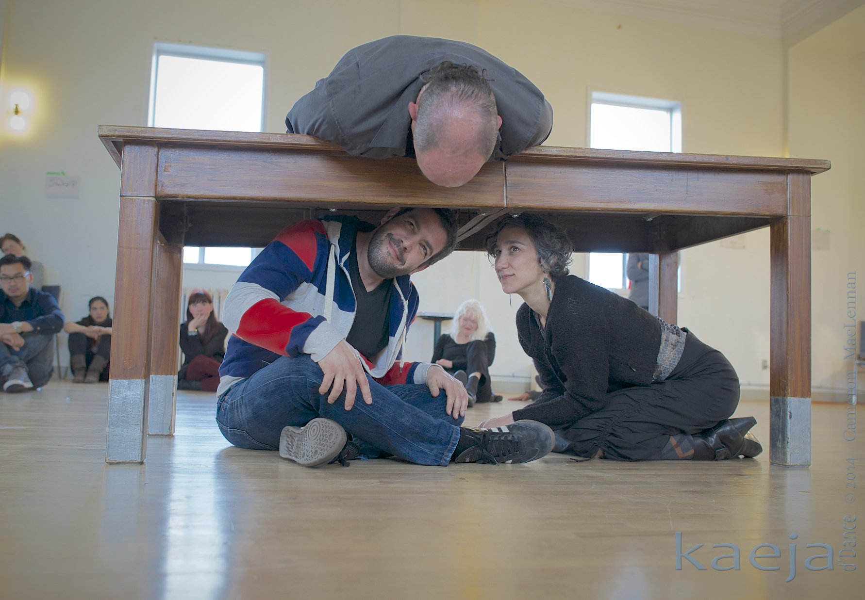 Allen lays on a table, peering at two people underneath it.