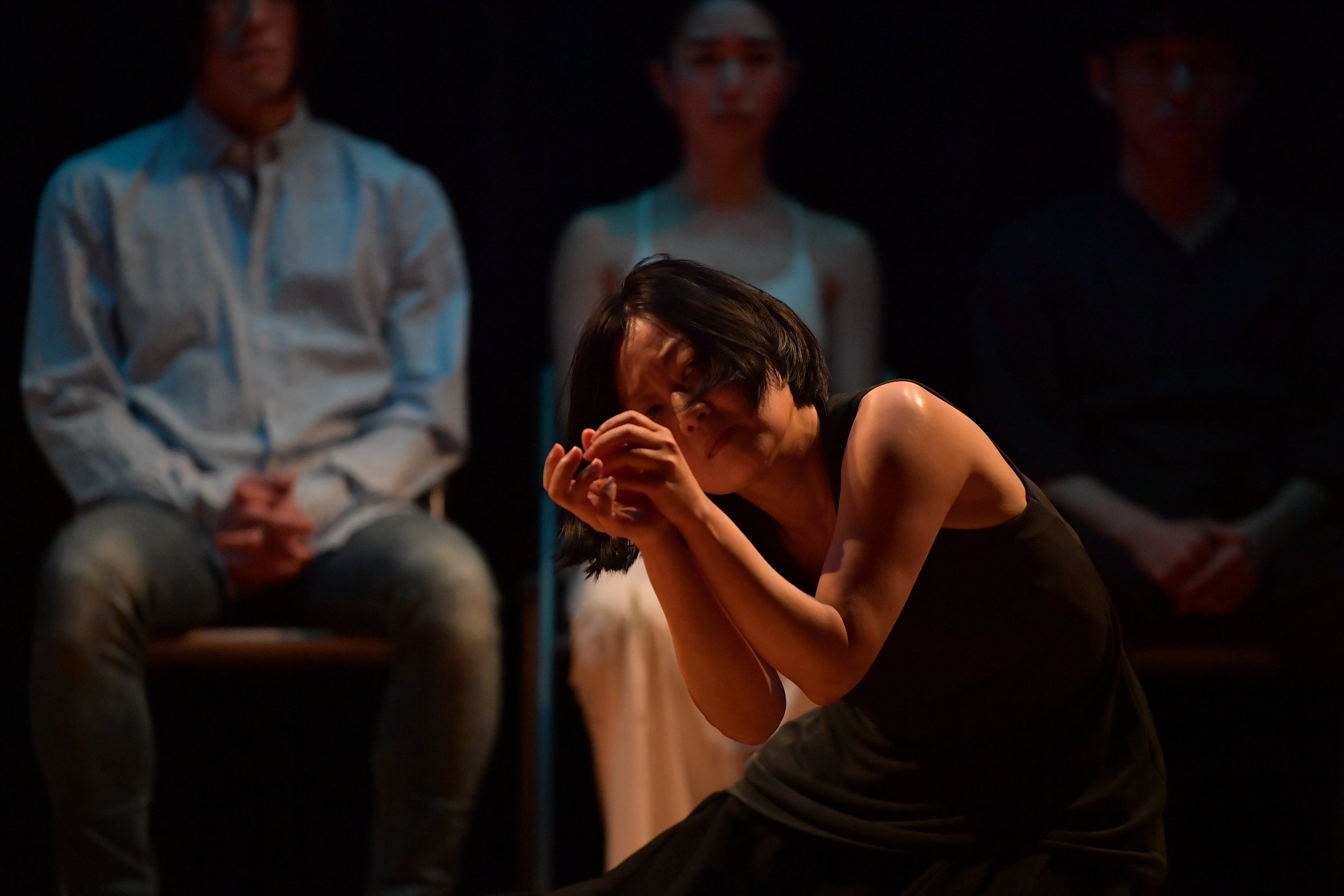 A dancer crouches, holding both hands in front of their face.
