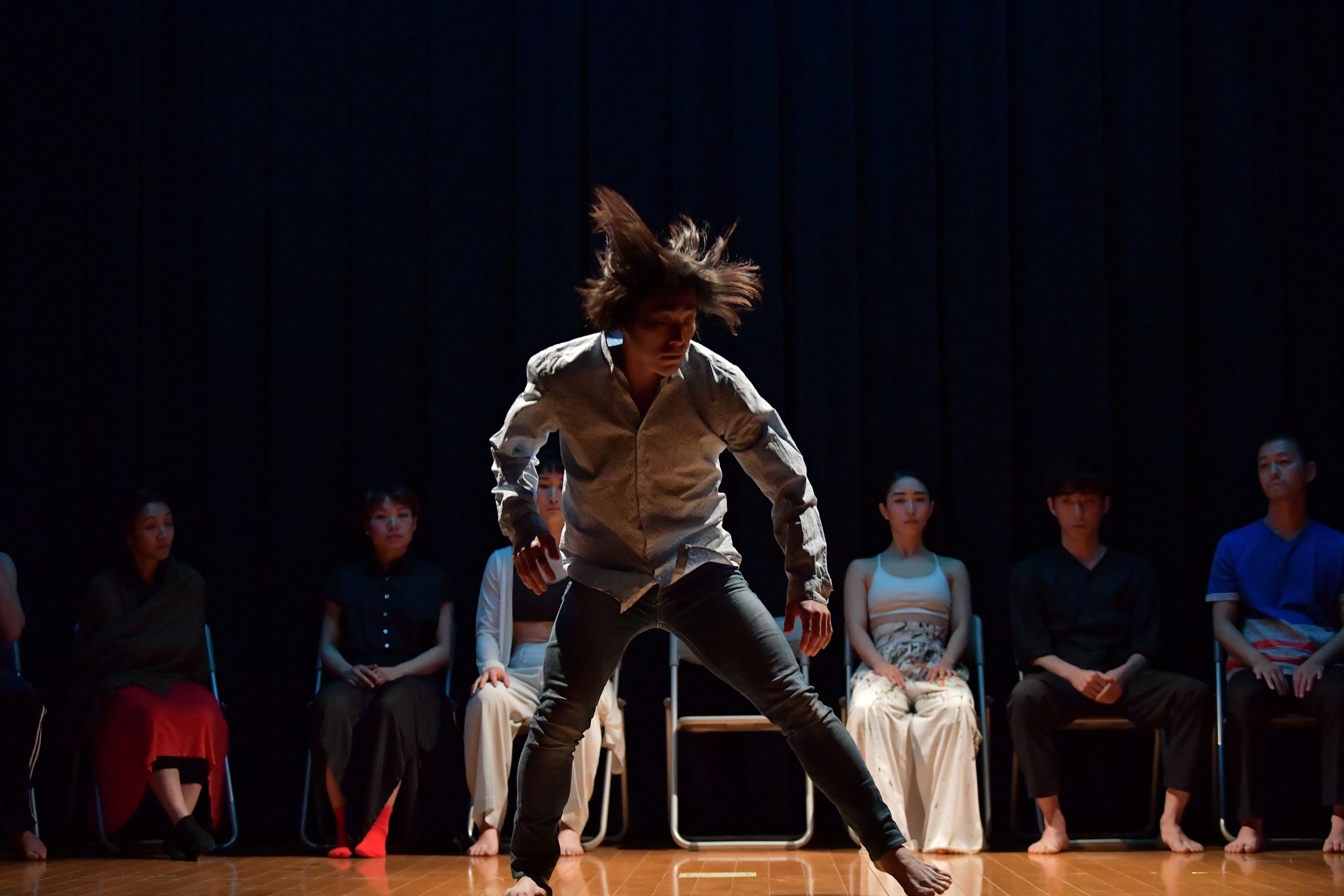 A dancer strikes a wide-legged stance, their hair flying as they move.