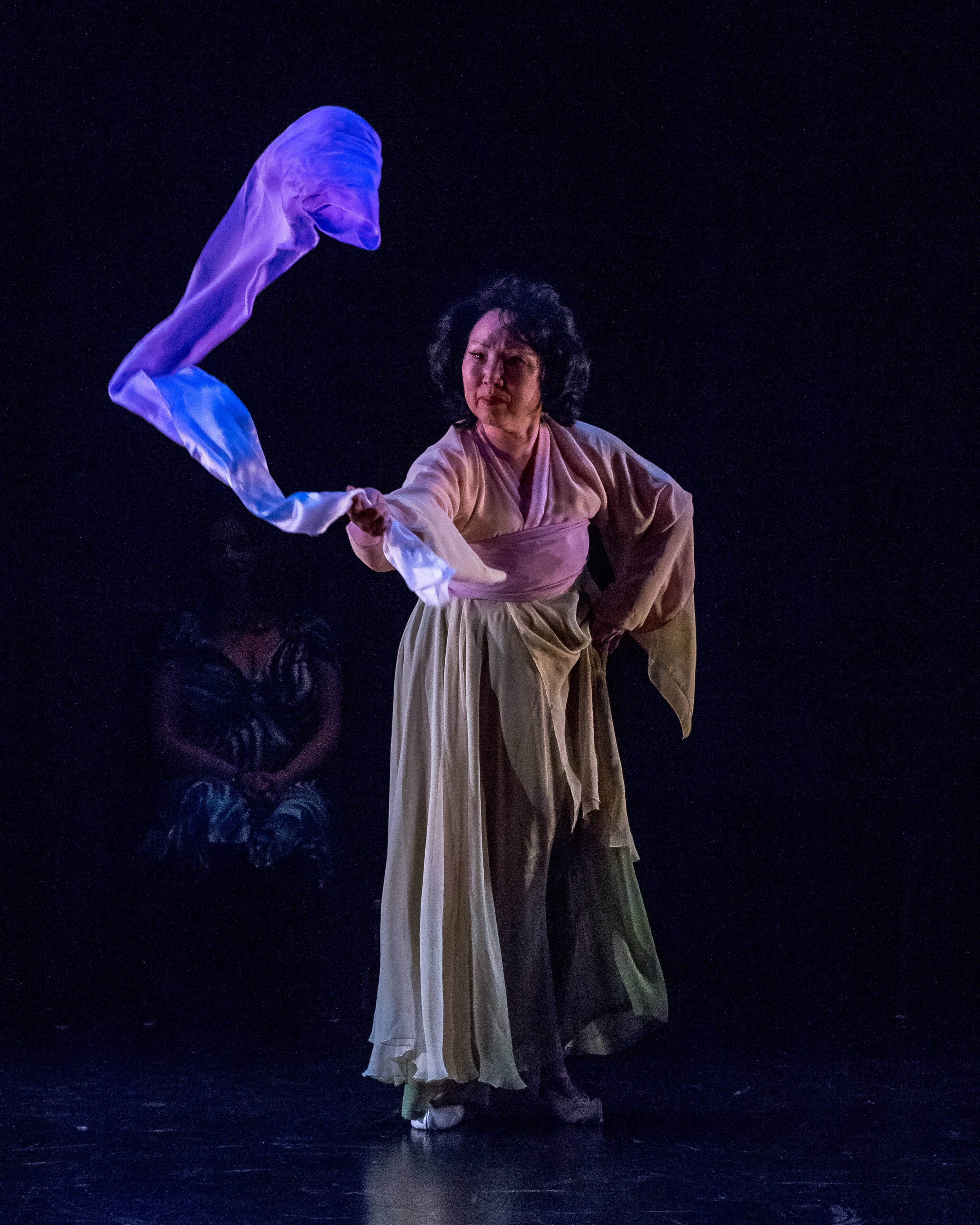 A dancer moves a long piece of fabric in the air in front of them.