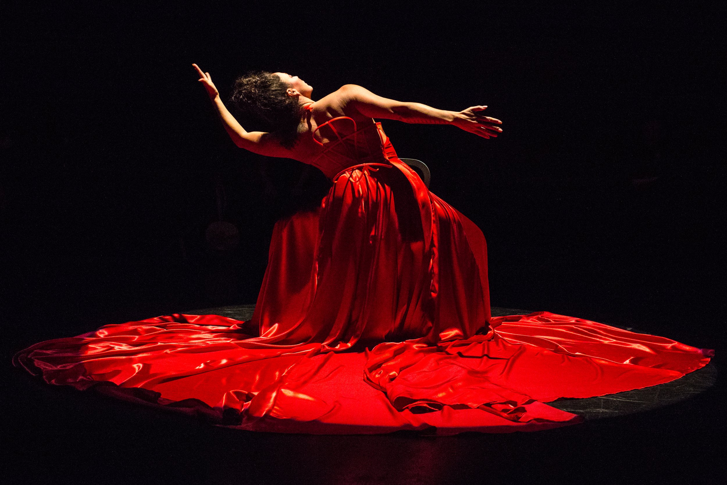 A dancer in a red dress with a huge skirt bends to one side, extending their arms in opposite directions.