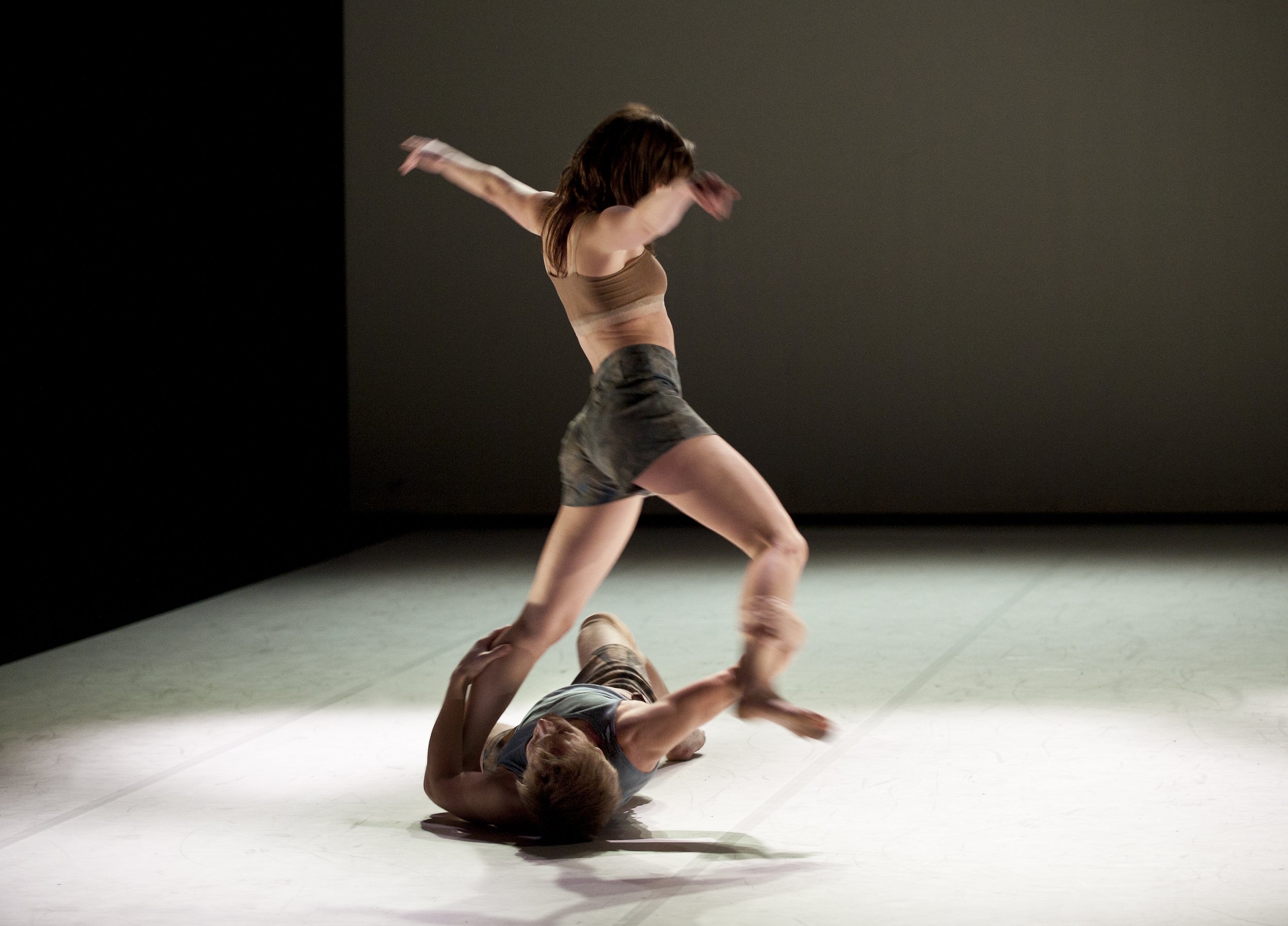 A dancer lies on the ground, grabbing the feet of another dancer.
