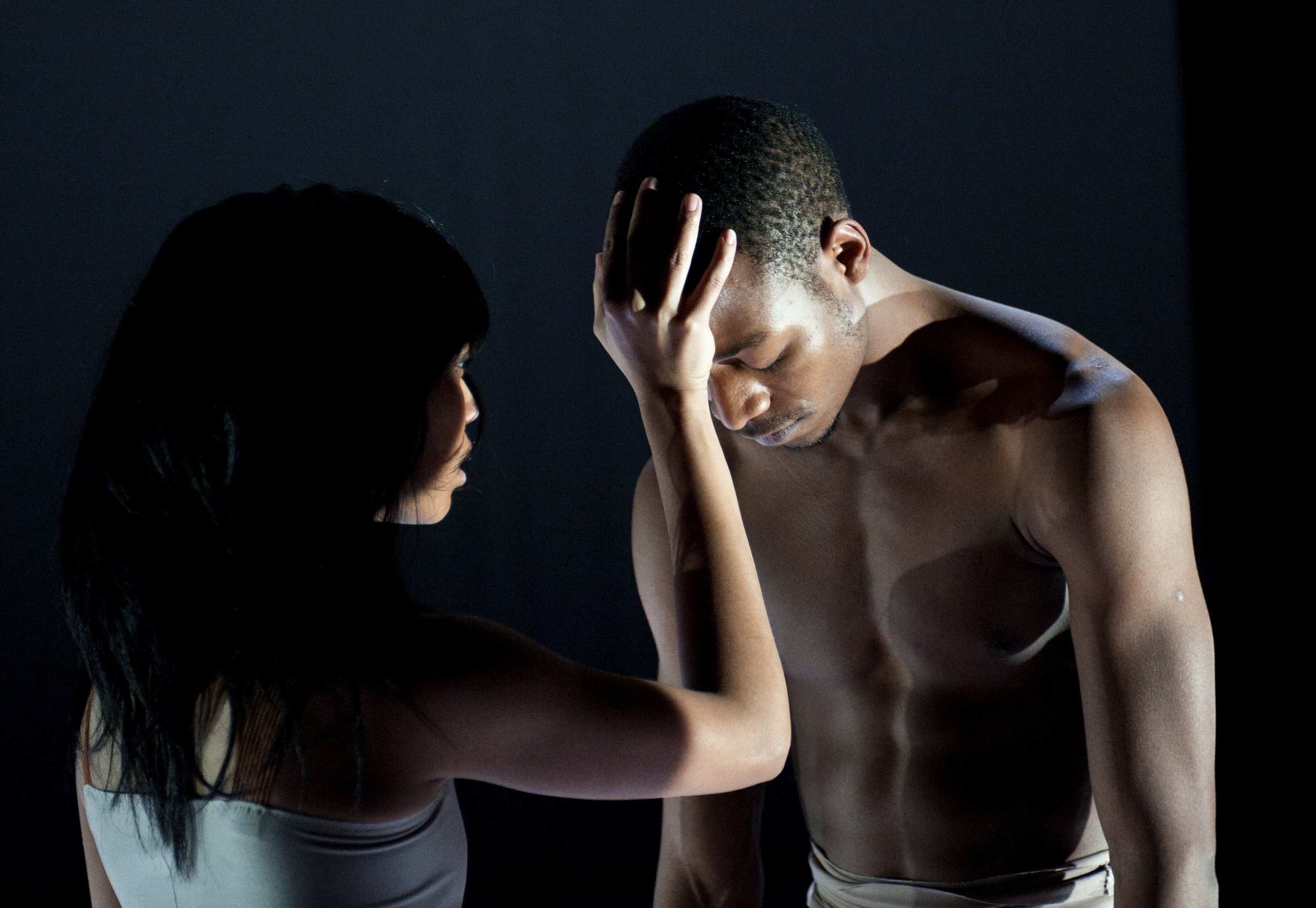 One dancer rests their forehead against the hand of another dancer.