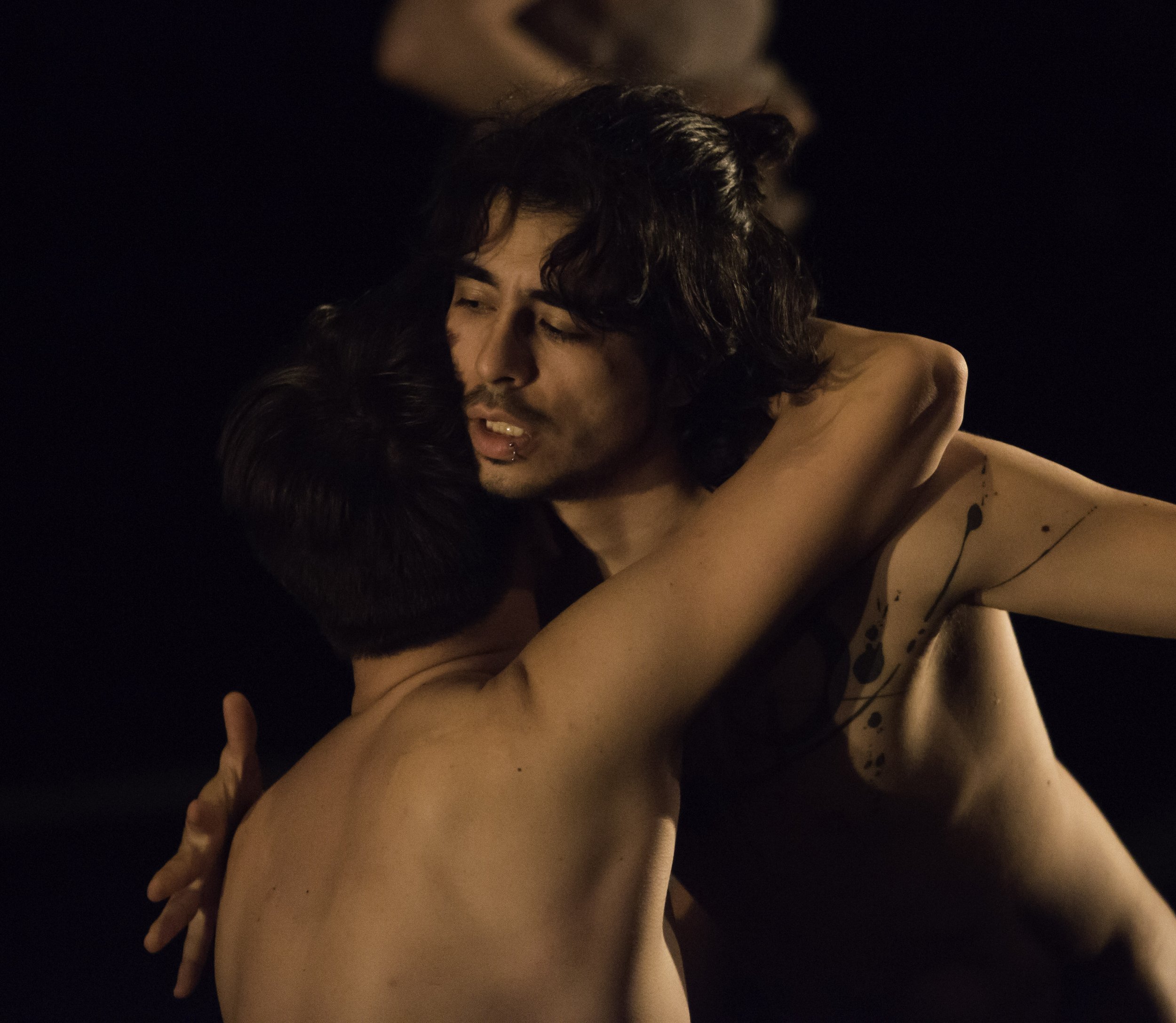 Two shirtless dancers embrace.