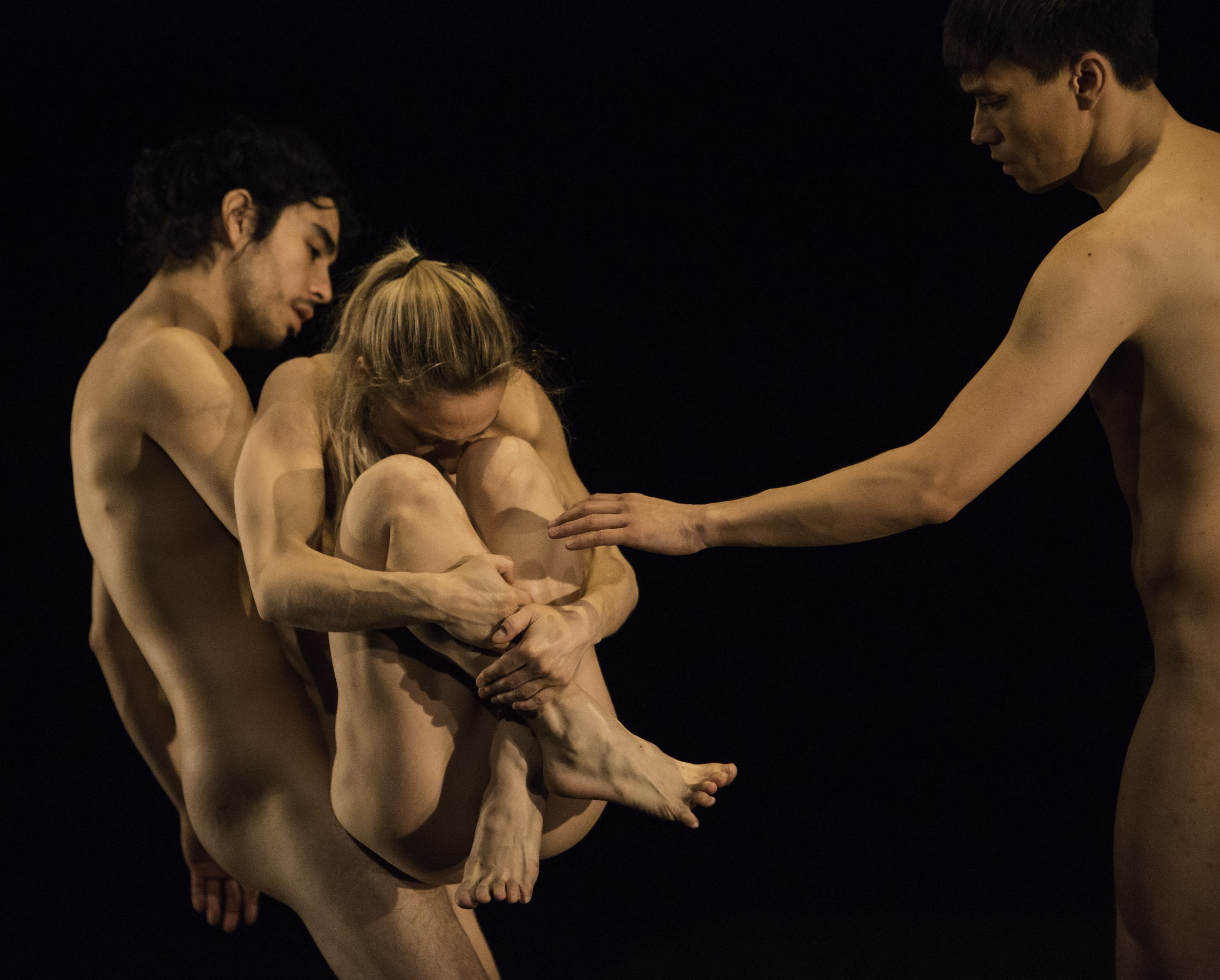 Three naked dancers; one carries another who is curled up into a ball, the third reaches to the one being carried with one hand.