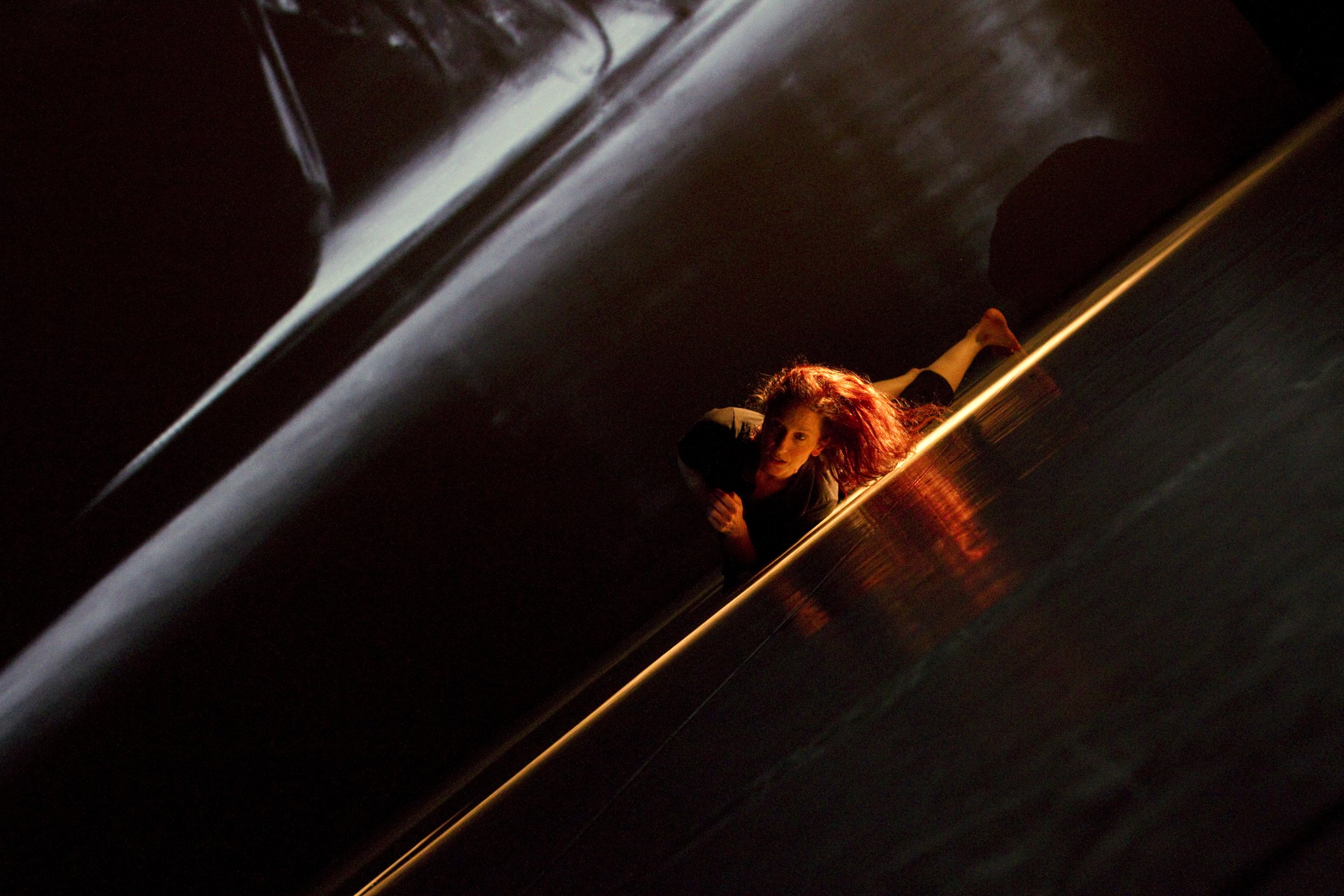A dancer rolls on the stage in a sliver of light.