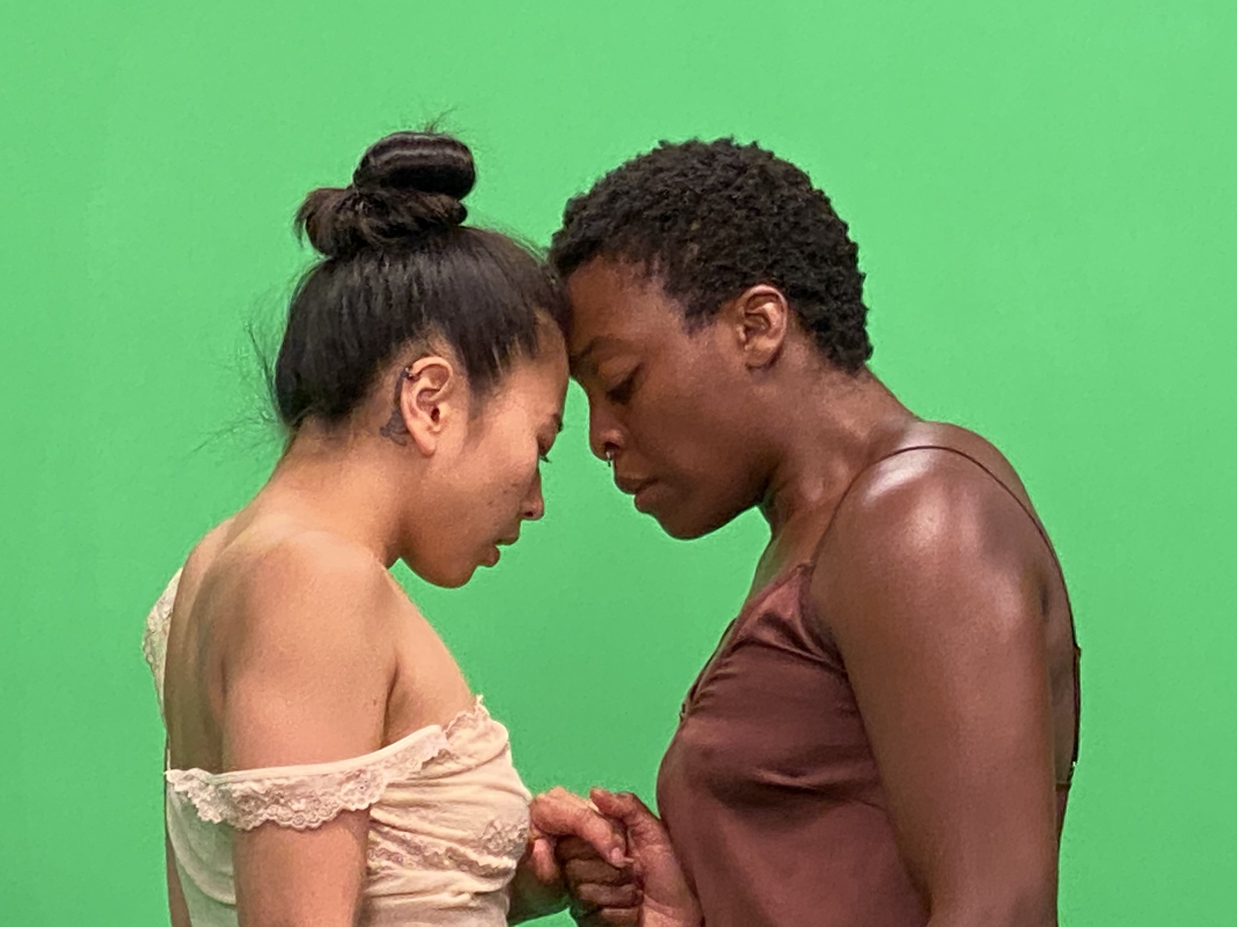 Two dancers touch foreheads in front of a green screen