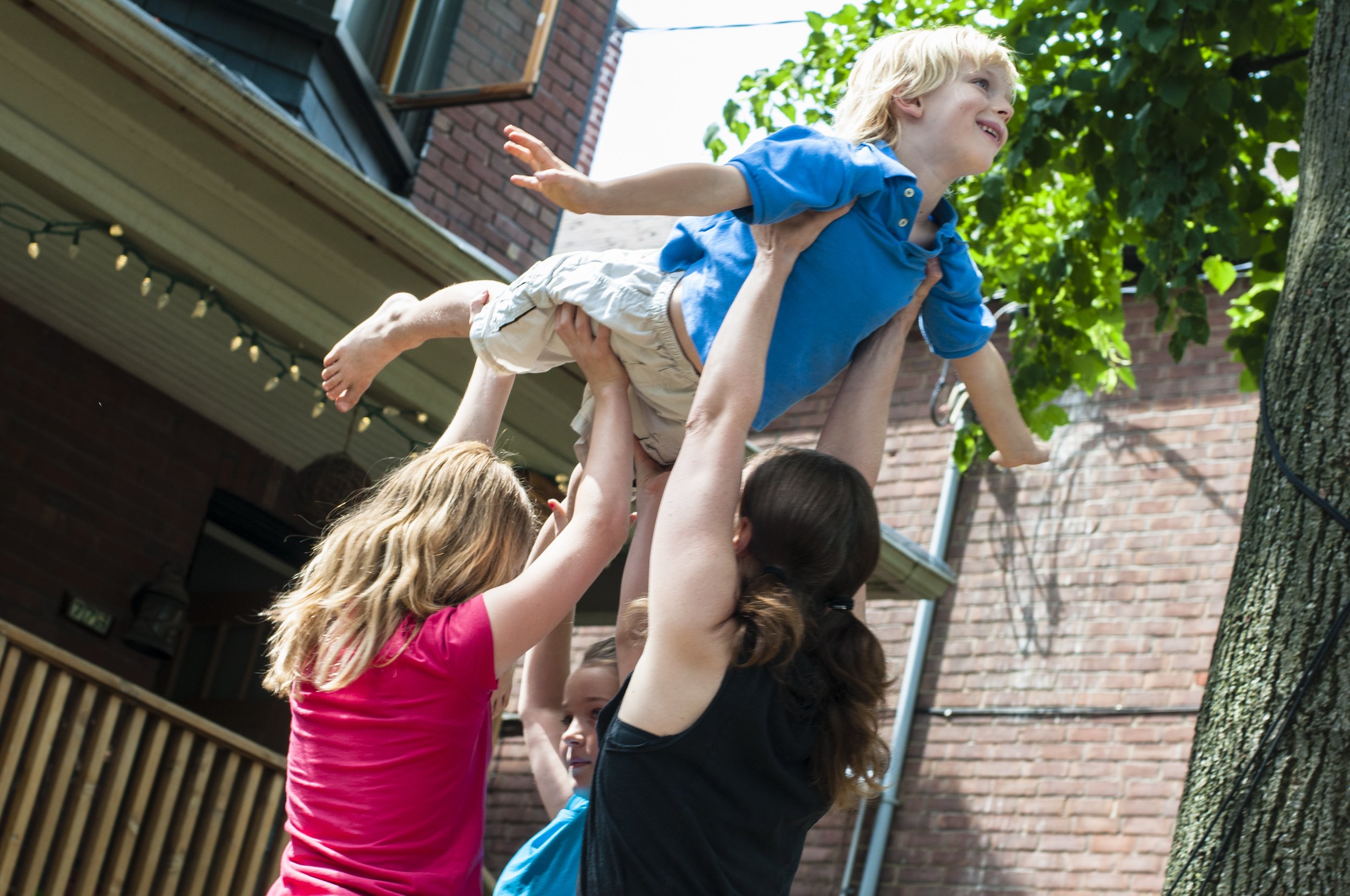 Several community participants lift a young child over their heads; it looks like he's flying.