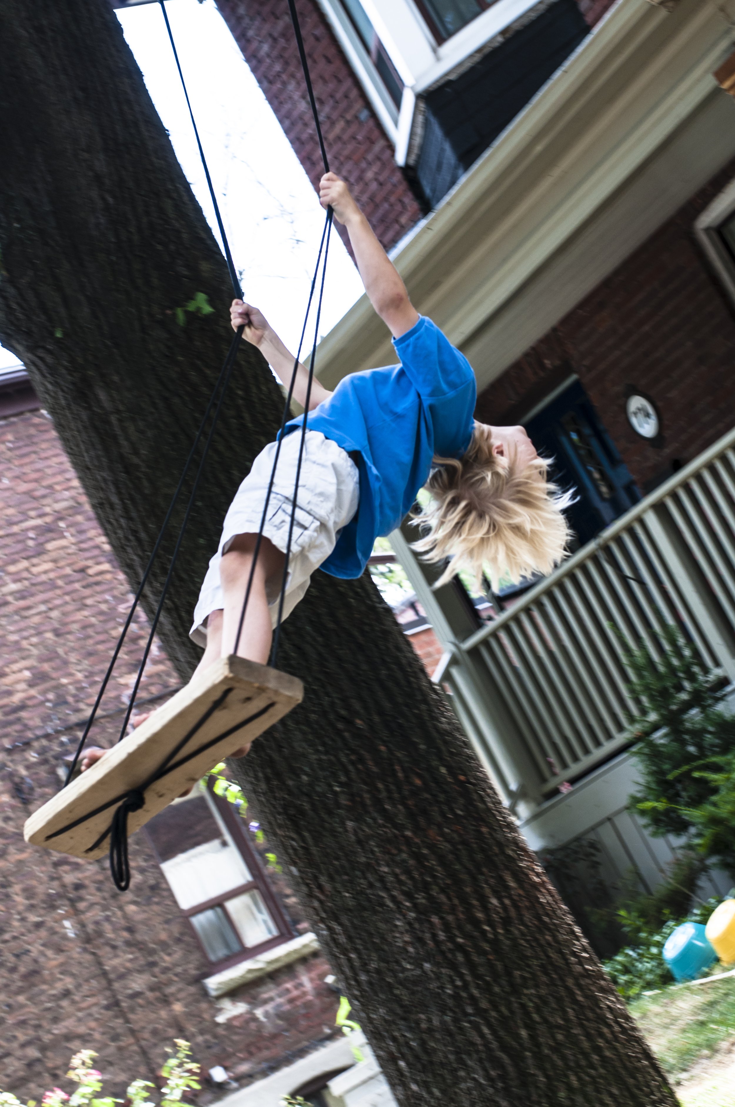 A young child stands on a swing in motion, leaning backwards.