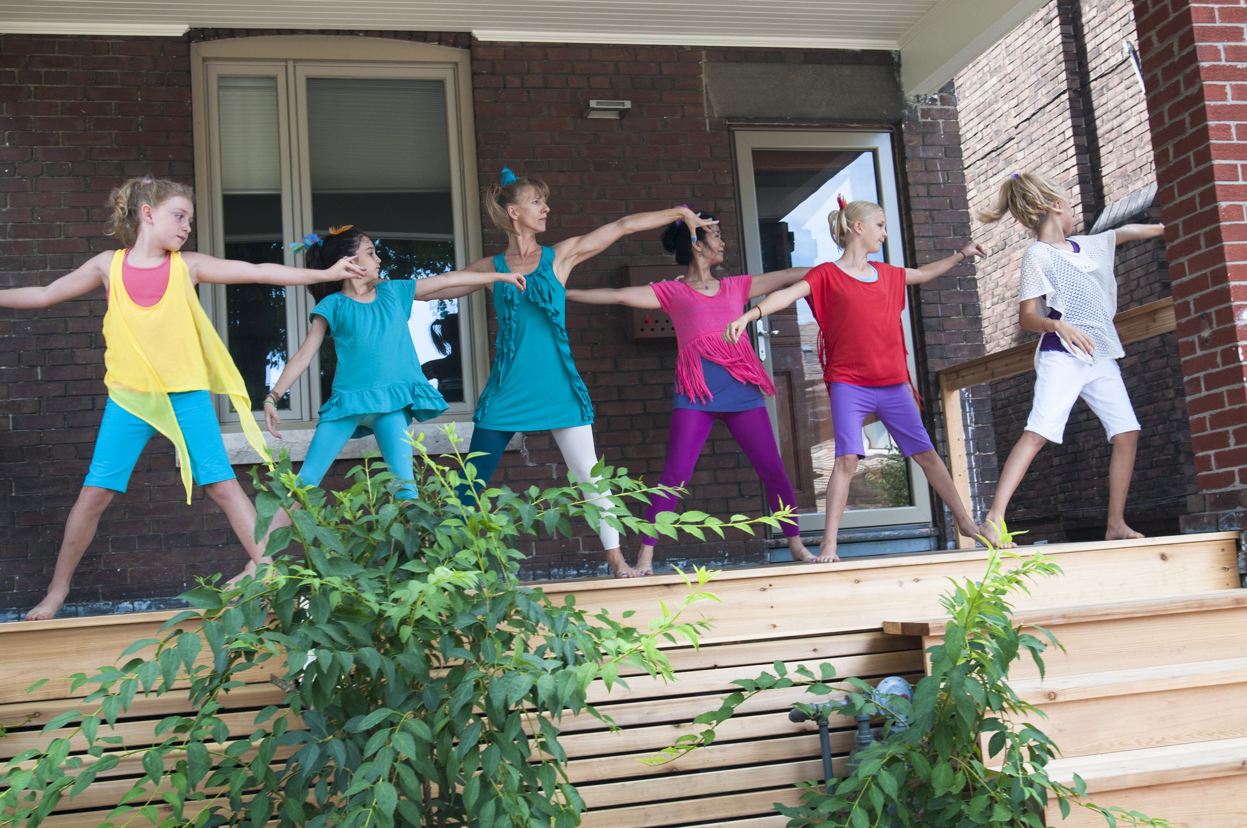 A group of young community participants on a porch with arms outstretched.
