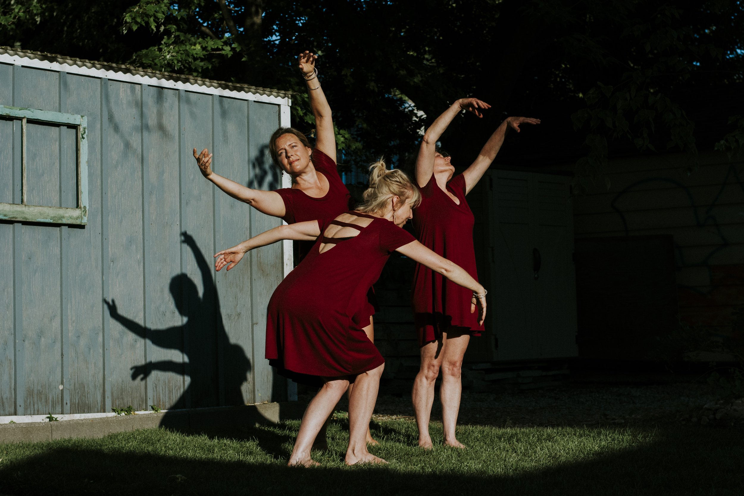 A trio of women wearing red dresses, dancing in a natural spotlight