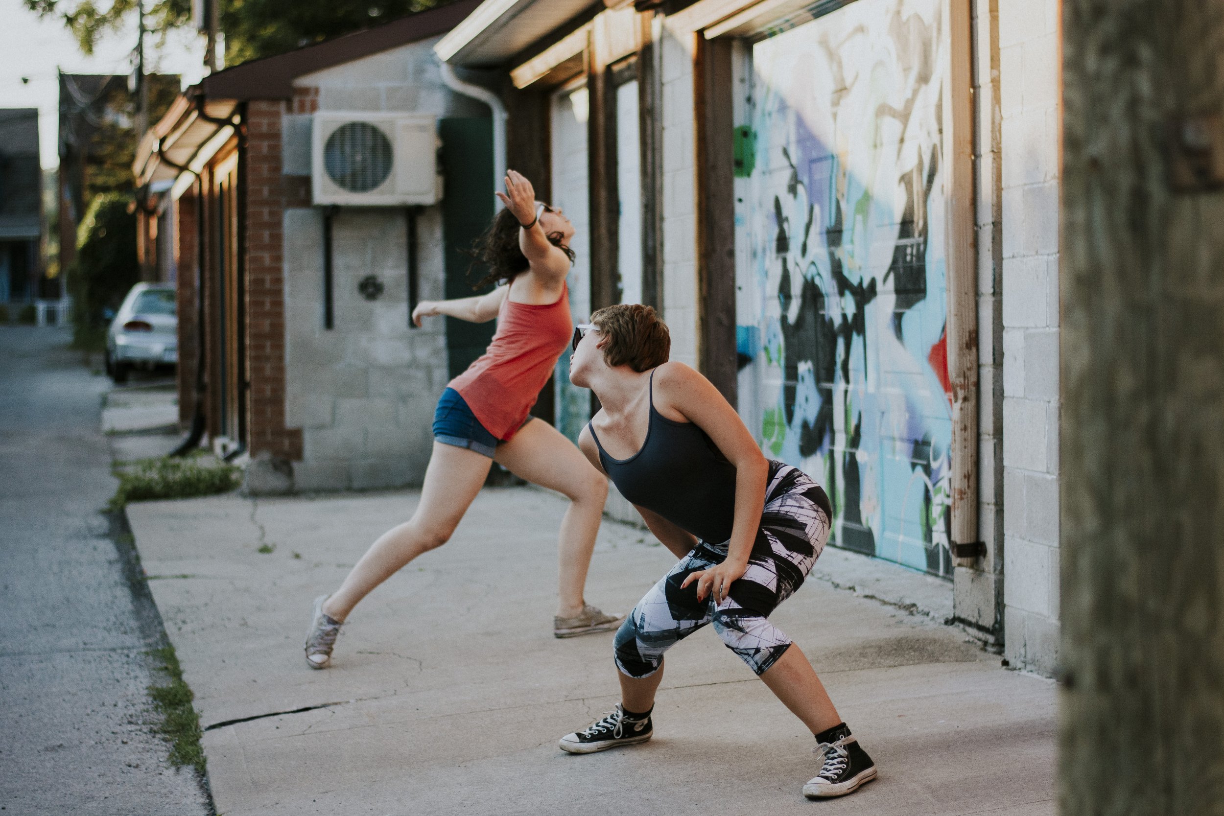 Two dancers, performing in front of a graffiti mural