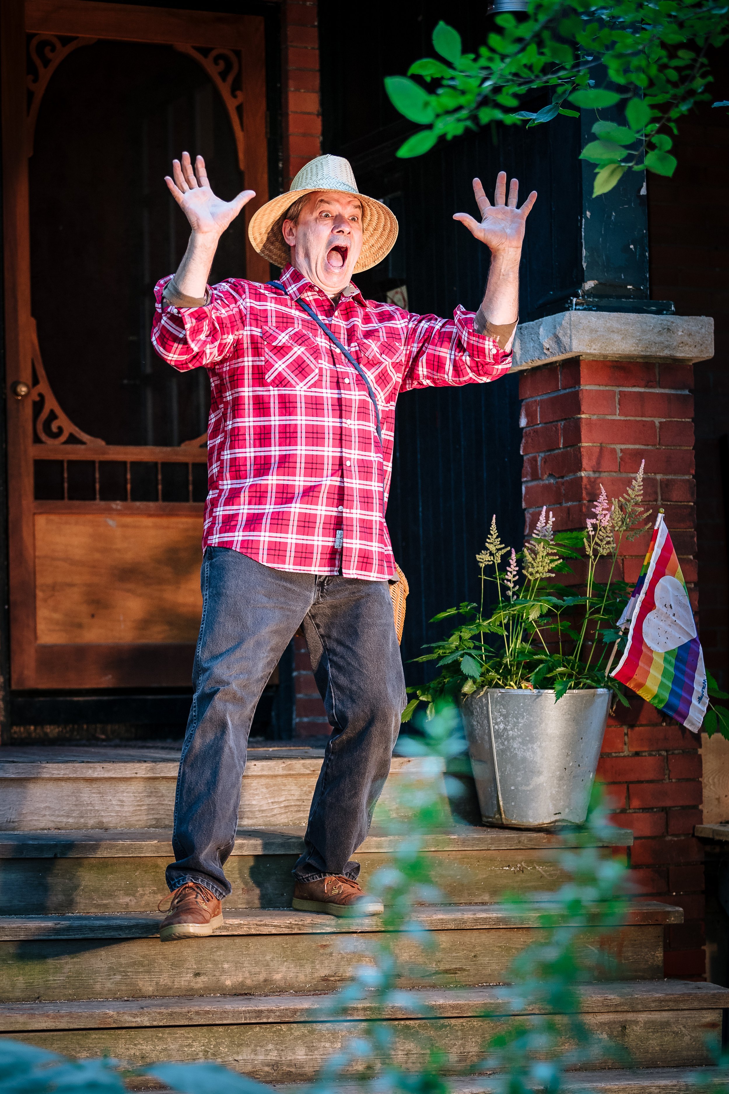 Man in a straw hat stands on the stairs, with loud expression on his face