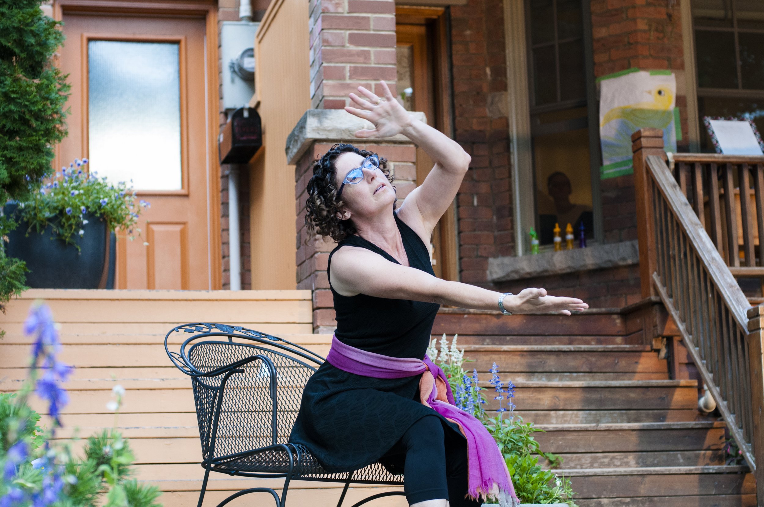 Woman dressed in black, dancing, while she sits on a lawn chair,