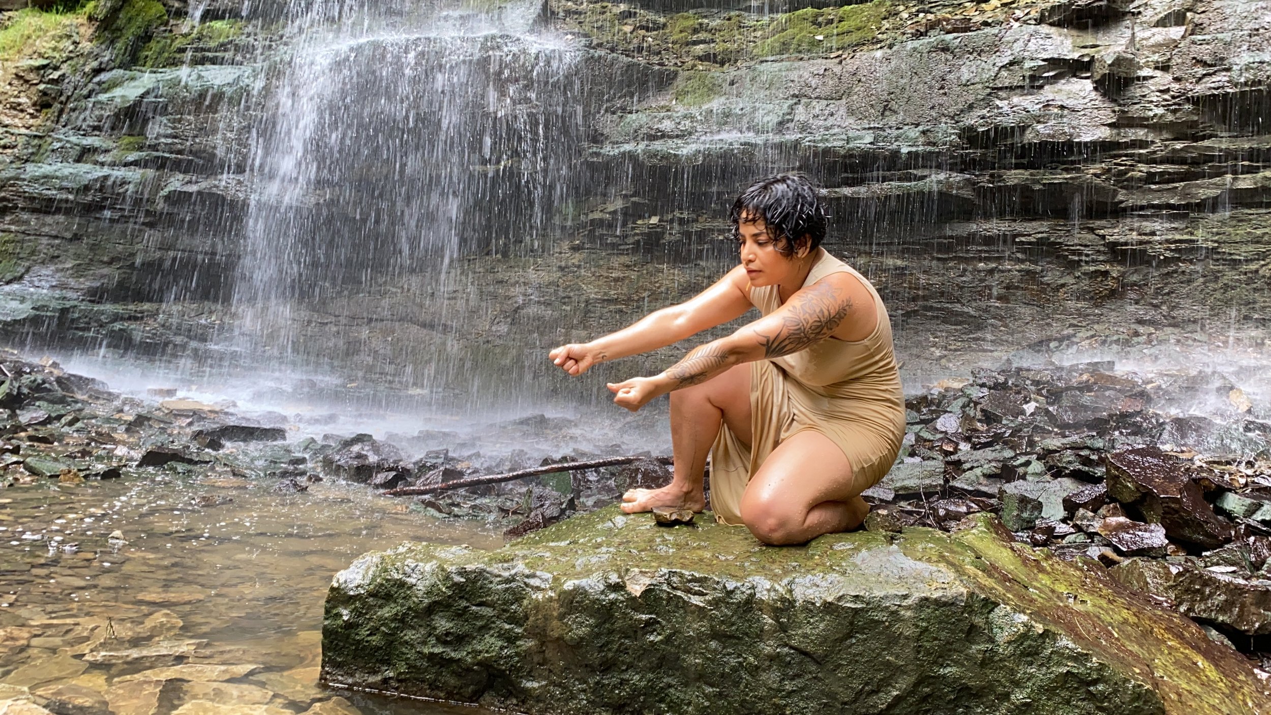 Woman kneeled on a rock in front of a small waterfall
