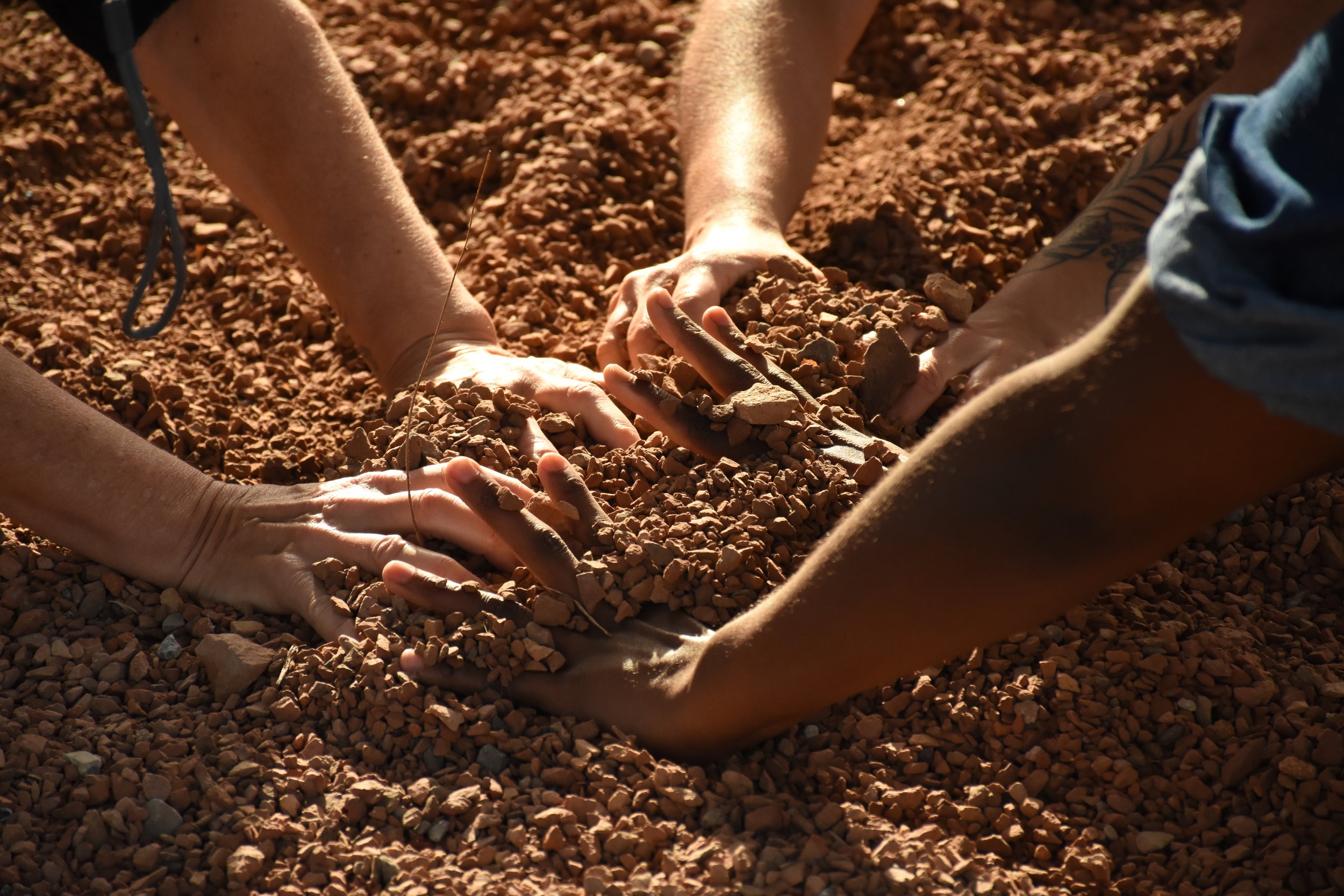Close up of three pairs of hands, each digging into gravel